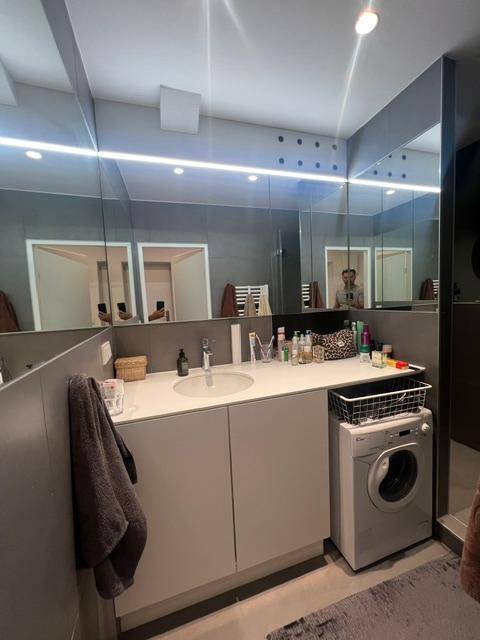 Modernes Badezimmer mit Einzelwaschbecken, großem Spiegelschrank und integrierter Waschmaschine.