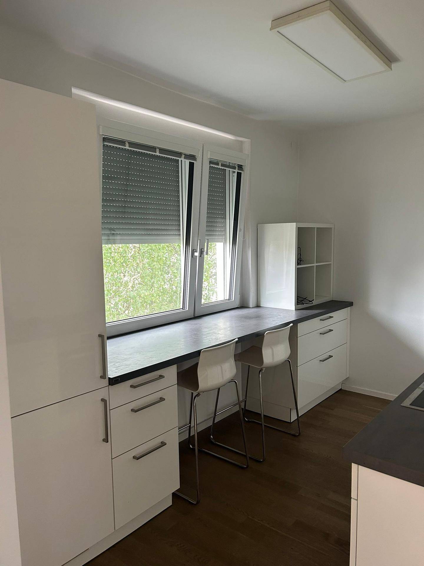 Helle Küche mit weißen Schränken, dunkler Arbeitsplatte und einem Essbereich an der Fensterbank.