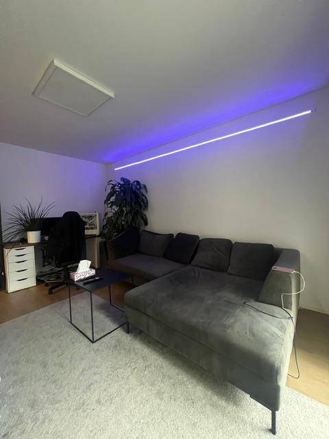 Modernes Wohnzimmer mit großem Ecksofa, Schreibtischbereich und indirekter lila Beleuchtung.
