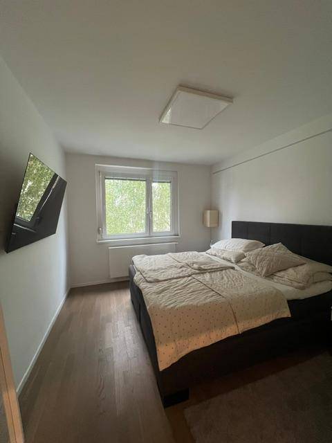 Gemütliches Schlafzimmer mit Doppelbett, Fenster und einem an der Wand montierten Fernseher.