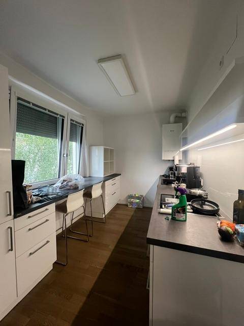 Funktionale Küche mit weißen Unterschränken, dunkler Arbeitsplatte und Fenster mit Rollladen.