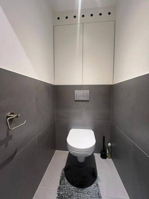 Separates WC mit wandhängender Toilette und modernen grauen Fliesen an den Wänden.