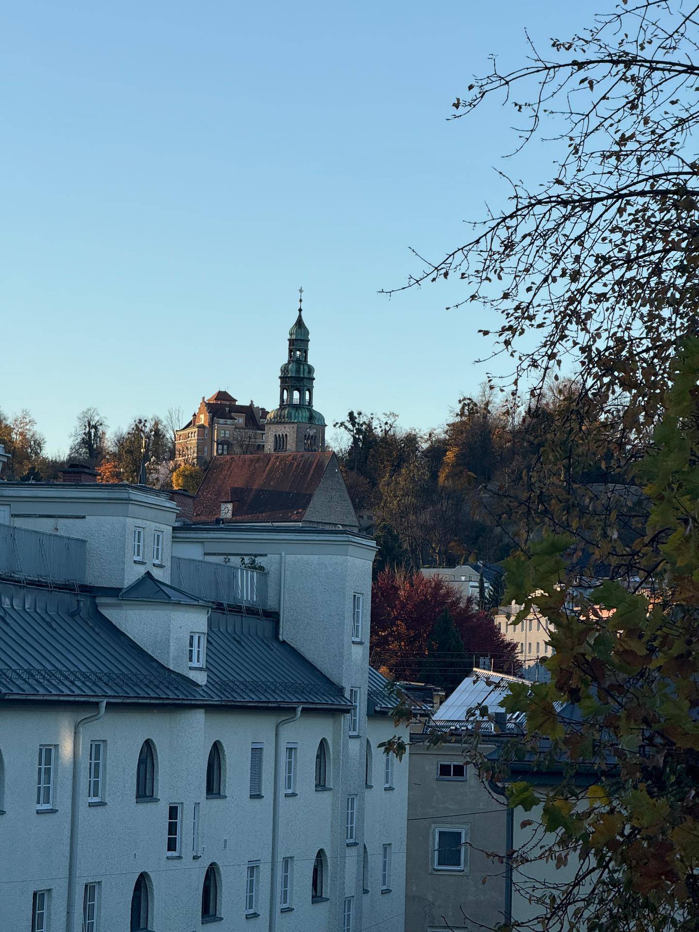 Malerischer Blick auf historische Gebäude und einen Kirchturm auf einem Hügel mit Herbstbäumen.
