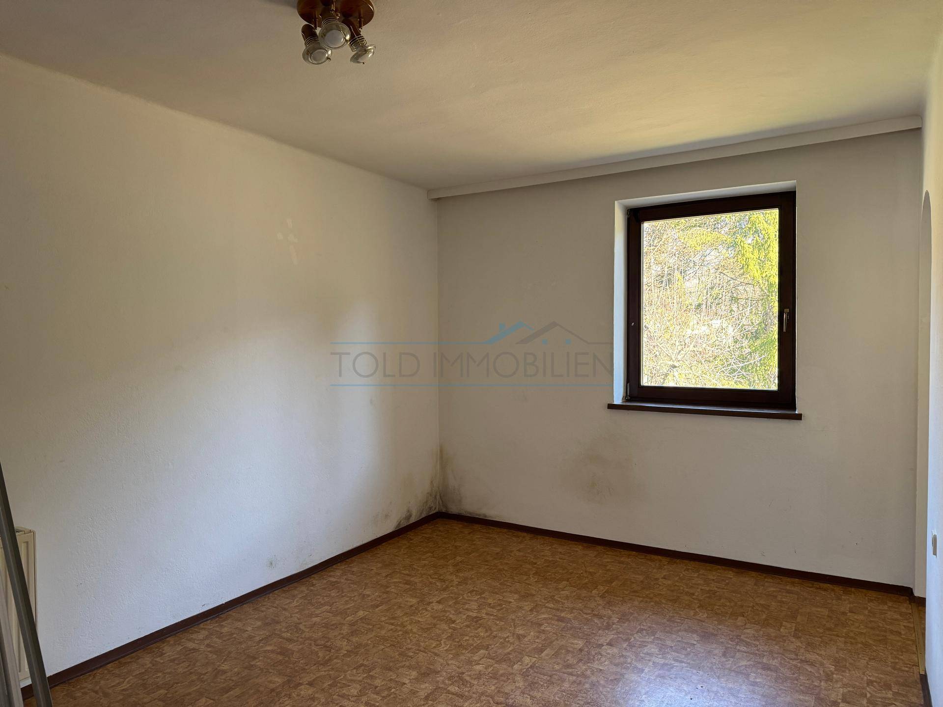 Schlafzimmer mit Korkboden und Fenster, das viel Tageslicht hereinlässt.