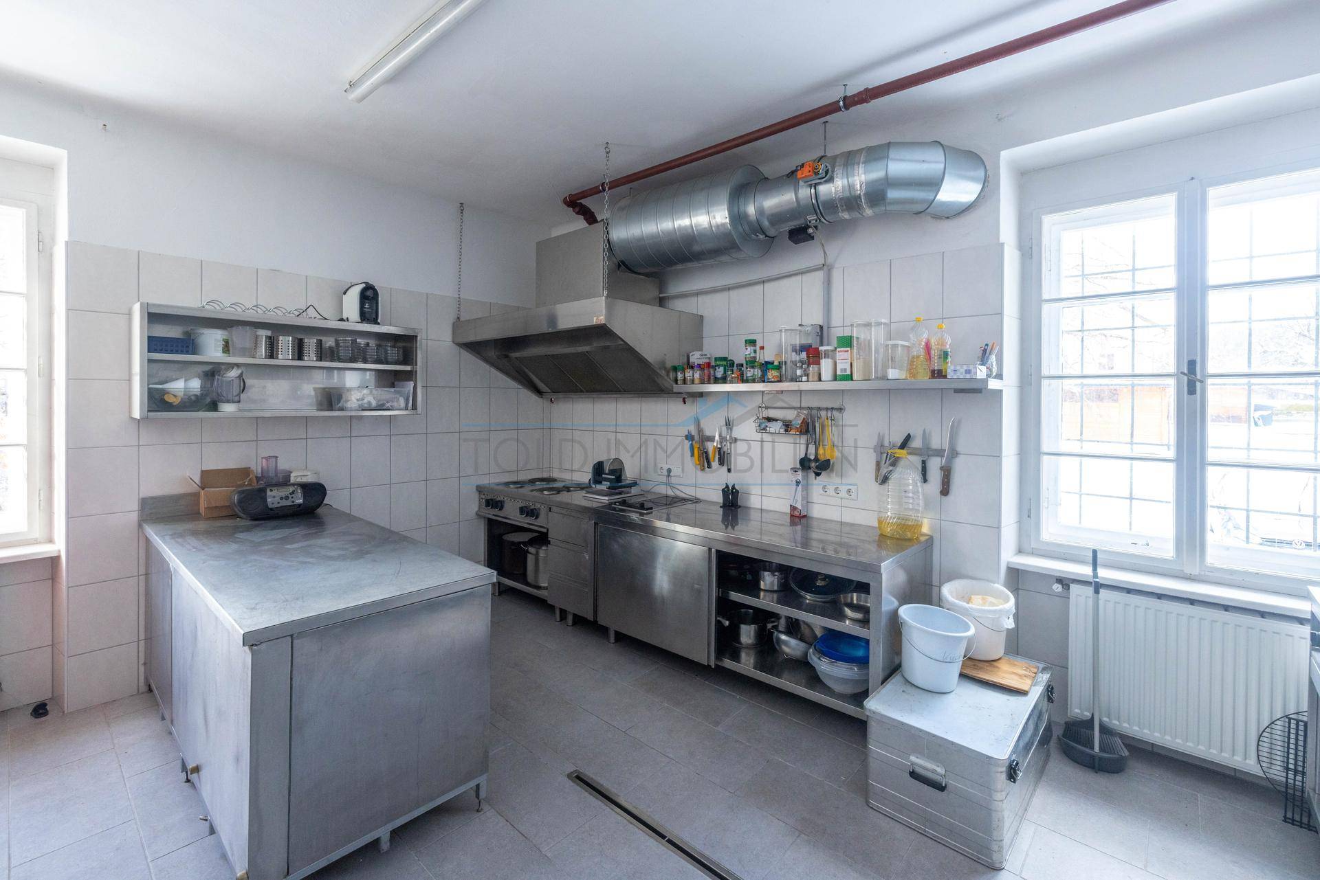 Industrielle Küche mit Edelstahlgeräten, Arbeitsflächen und professioneller Abluftanlage, ideal für Großküchen.
