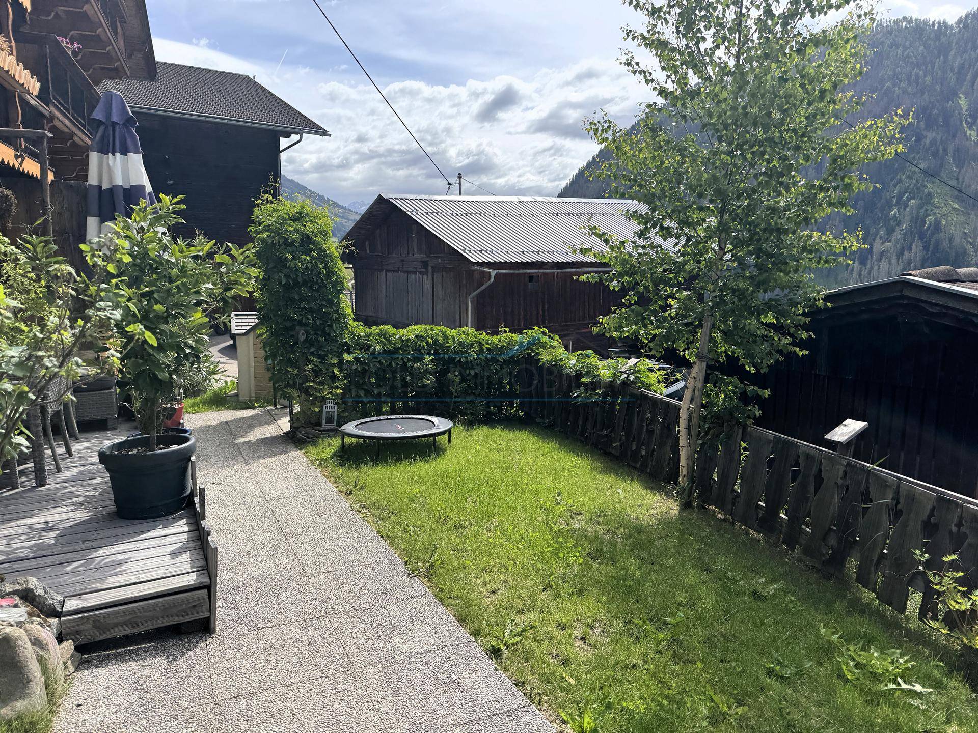 Kleiner Gartenbereich mit Rasenfläche, Trampolin und Blick auf die Berglandschaft.