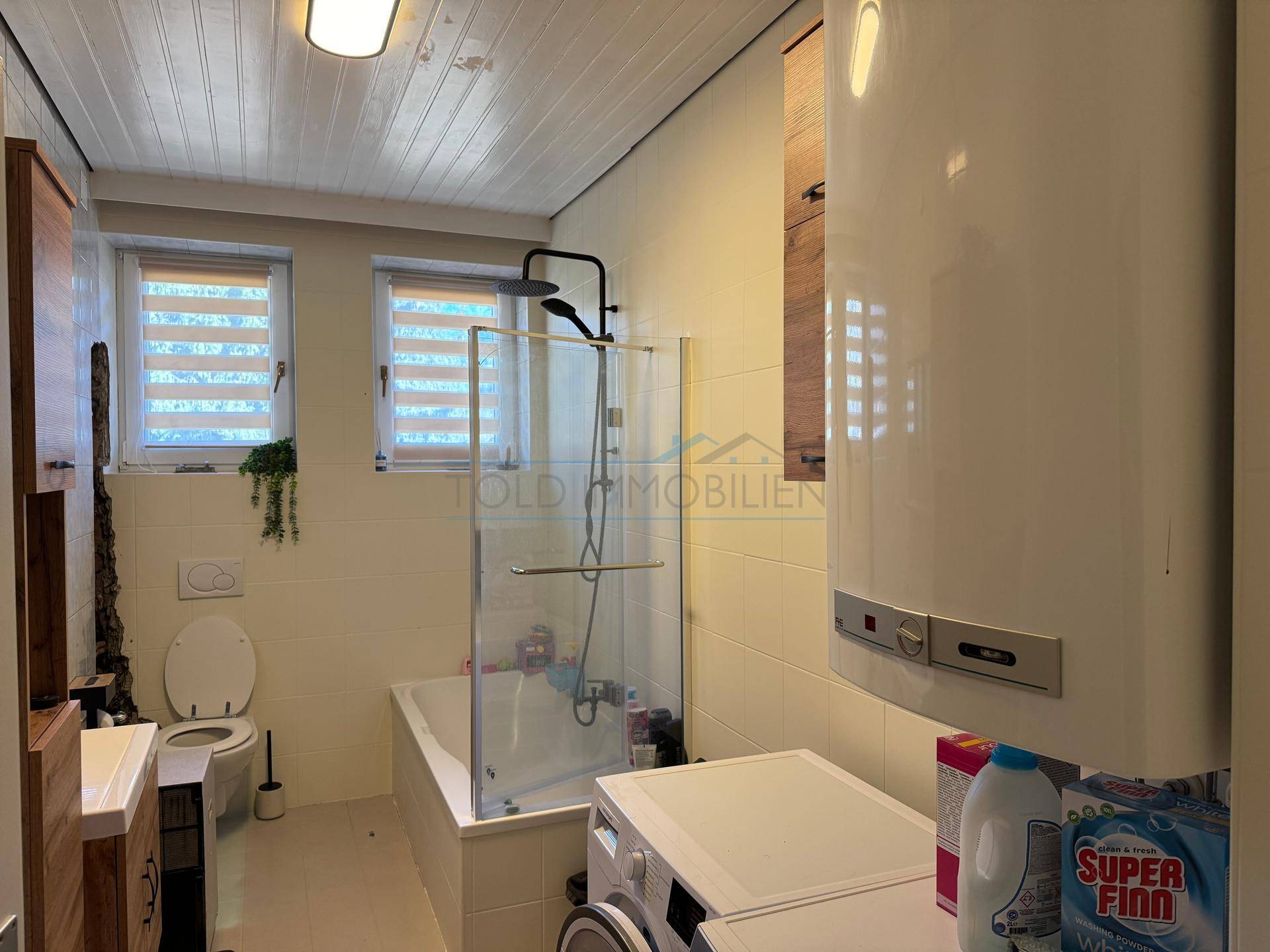 Badezimmer mit Badewanne, Duschabtrennung und Waschmaschine, gut beleuchtet.