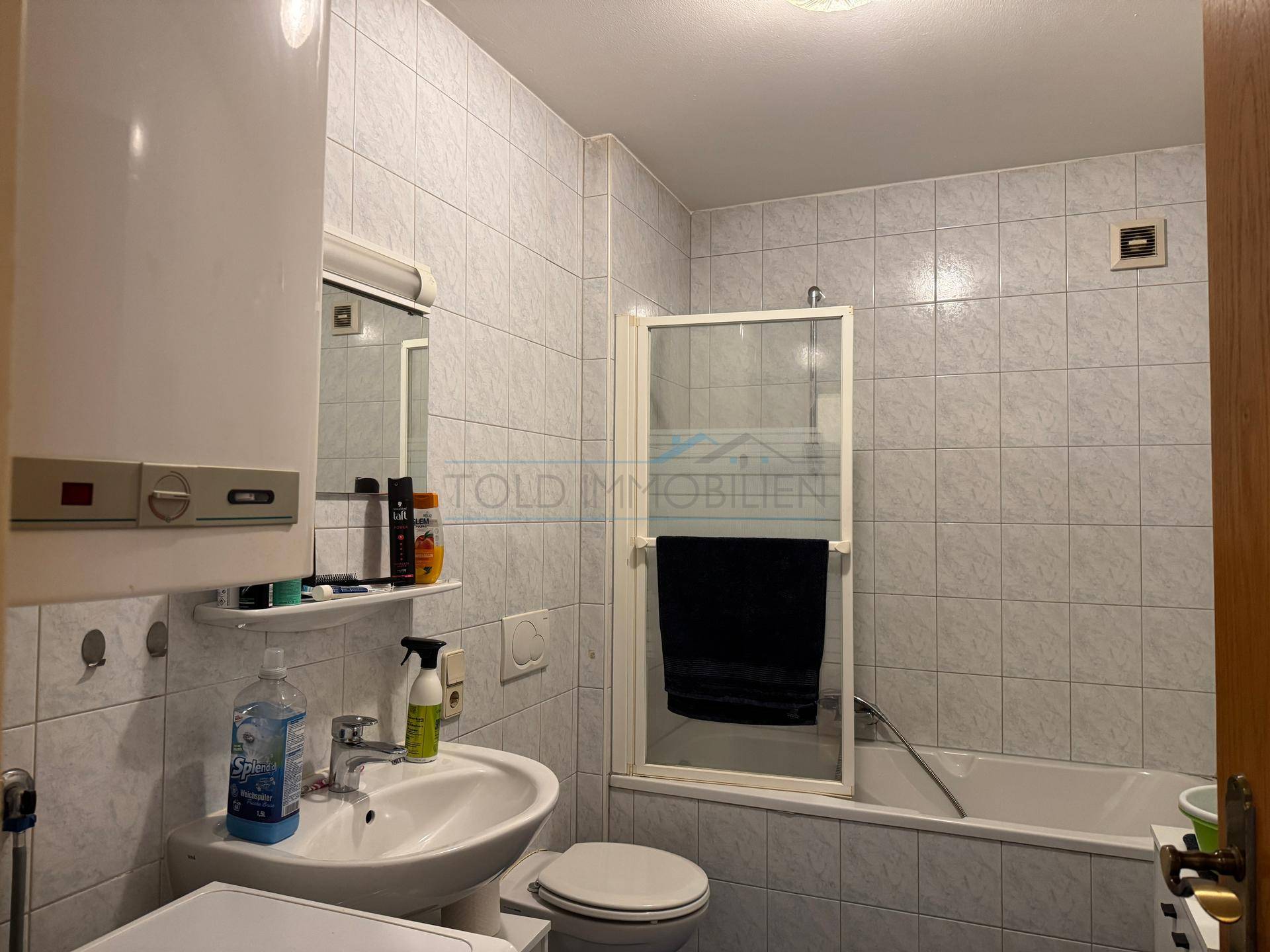 Badezimmer mit Badewanne, Duschvorrichtung und hellen Fliesen in gutem Zustand.