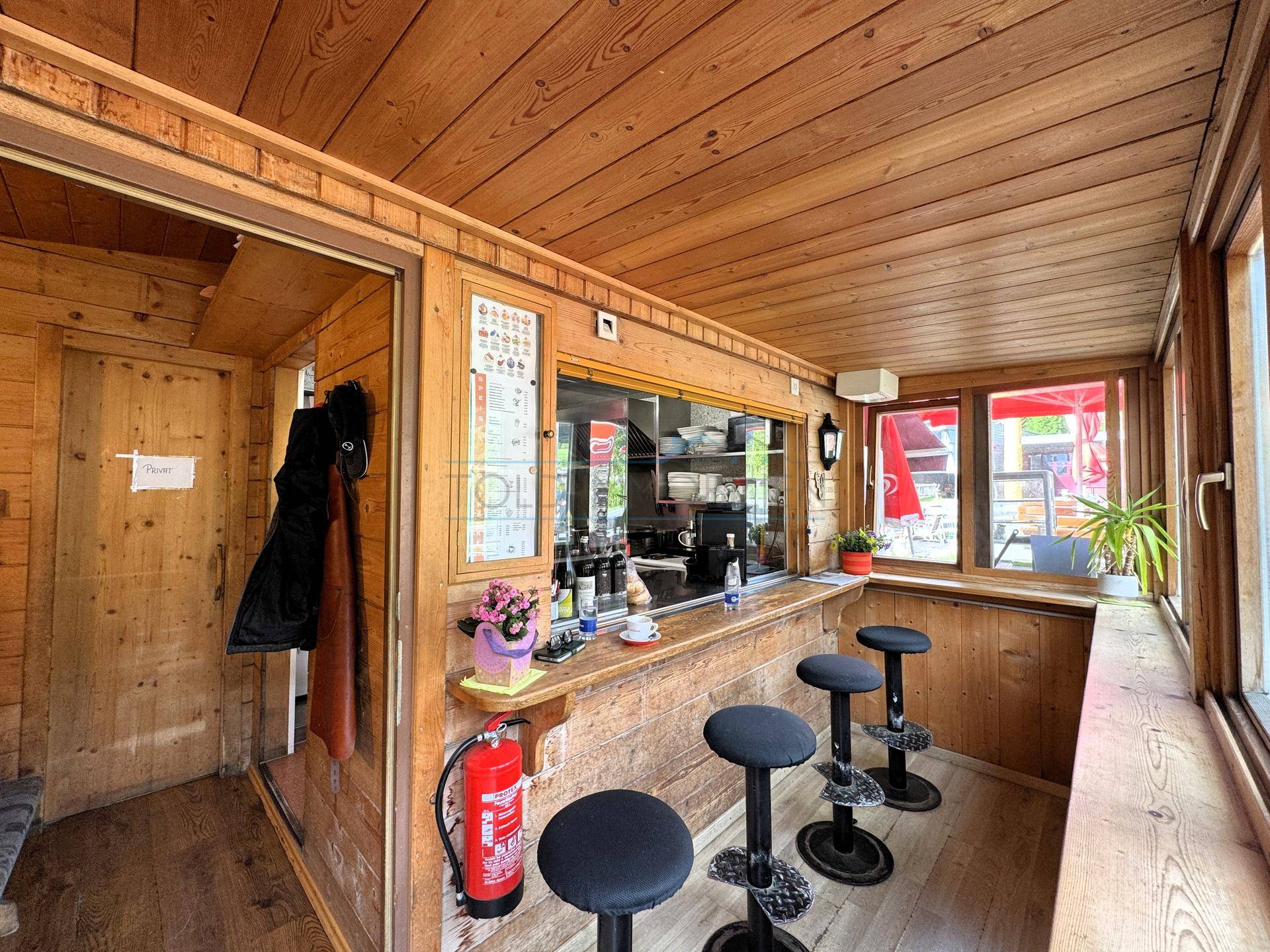 Rustikale Bar mit Holztäfelung, Theke und Barhockern, mit Blick auf die Außenterrasse.