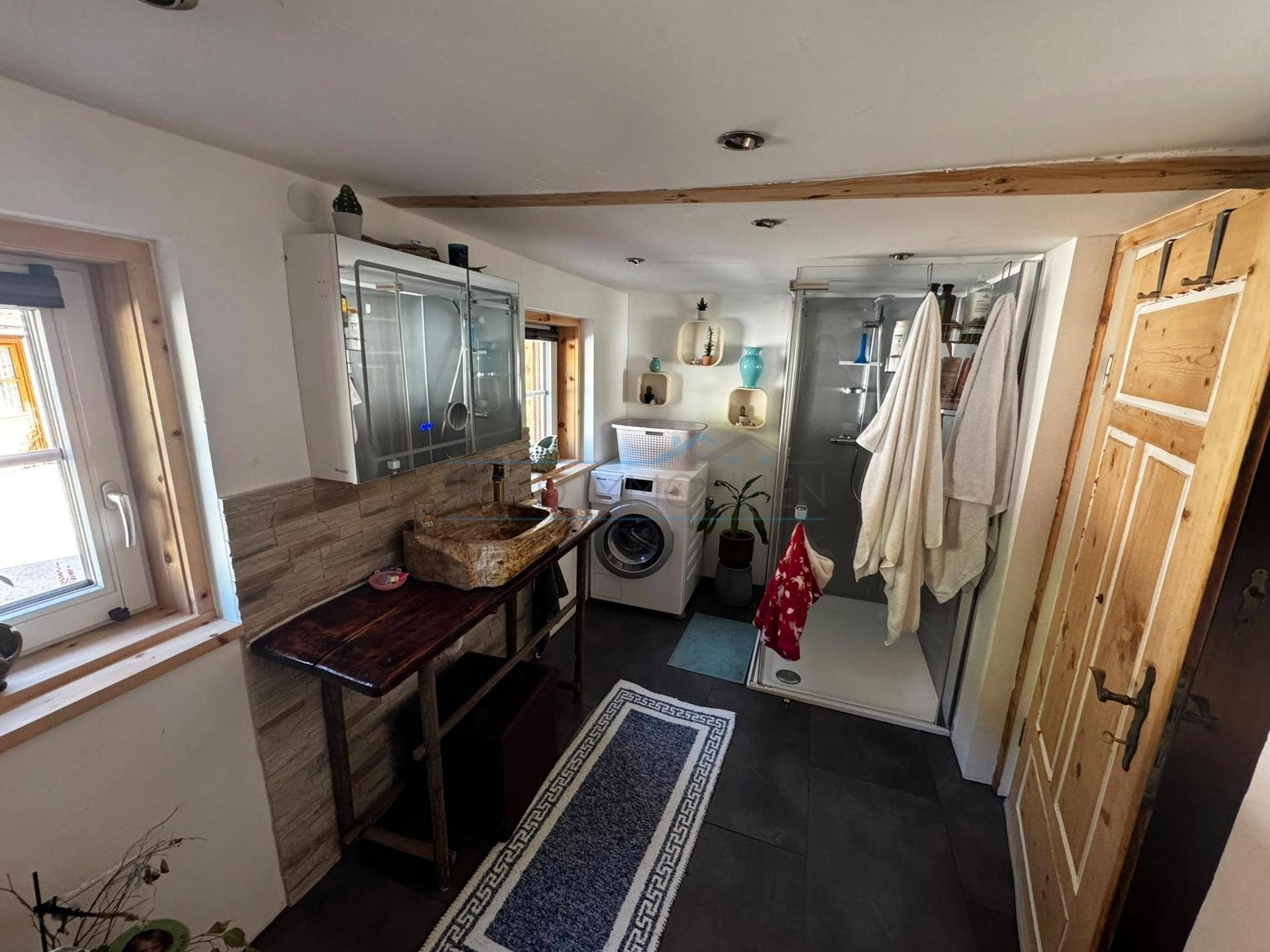 Modernisiertes Badezimmer mit Dusche, Waschmaschine und rustikalem Holzwaschtisch.