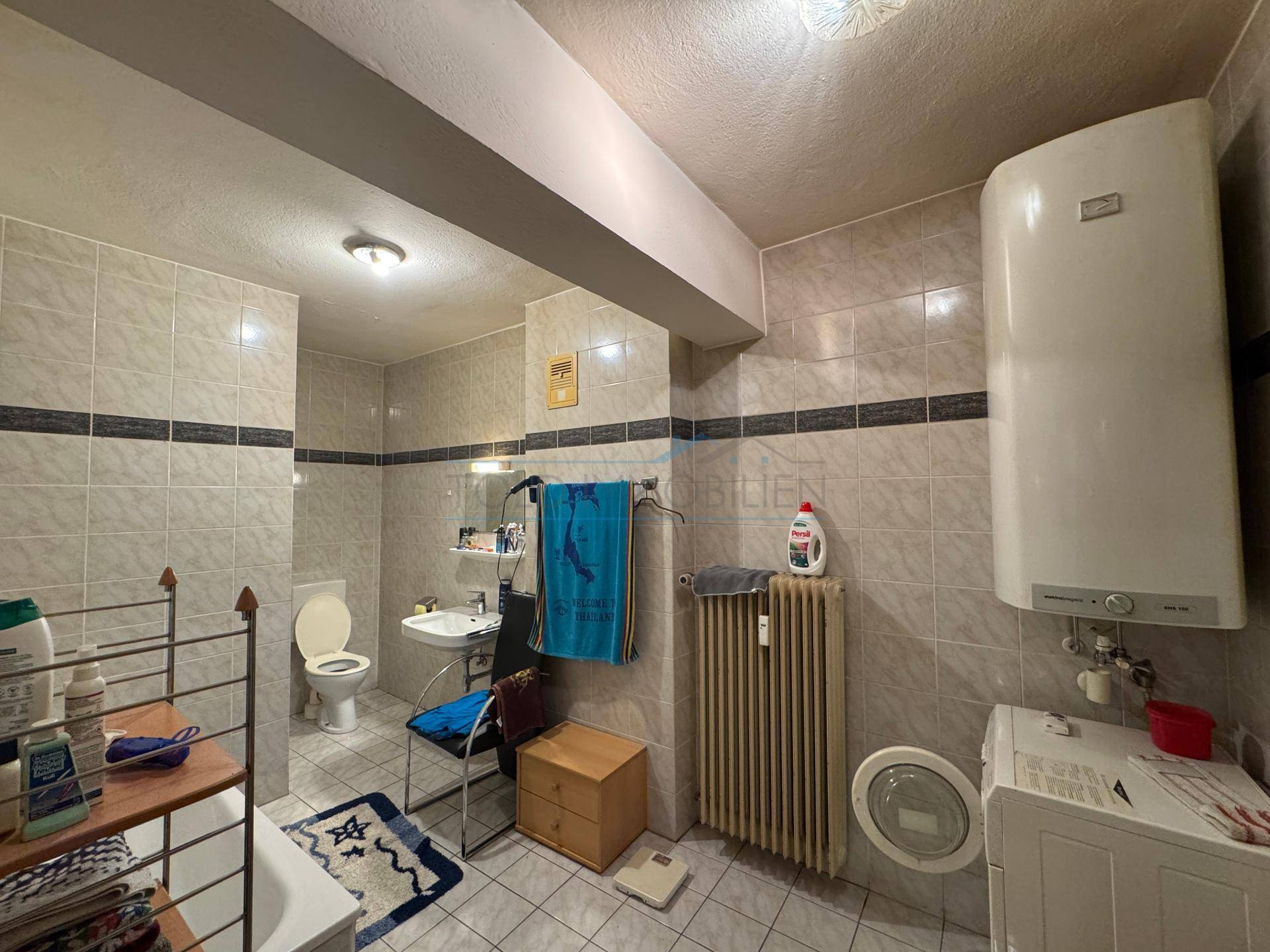 Geräumiges Badezimmer mit Badewanne, Waschbecken und Waschmaschine, gefliest.