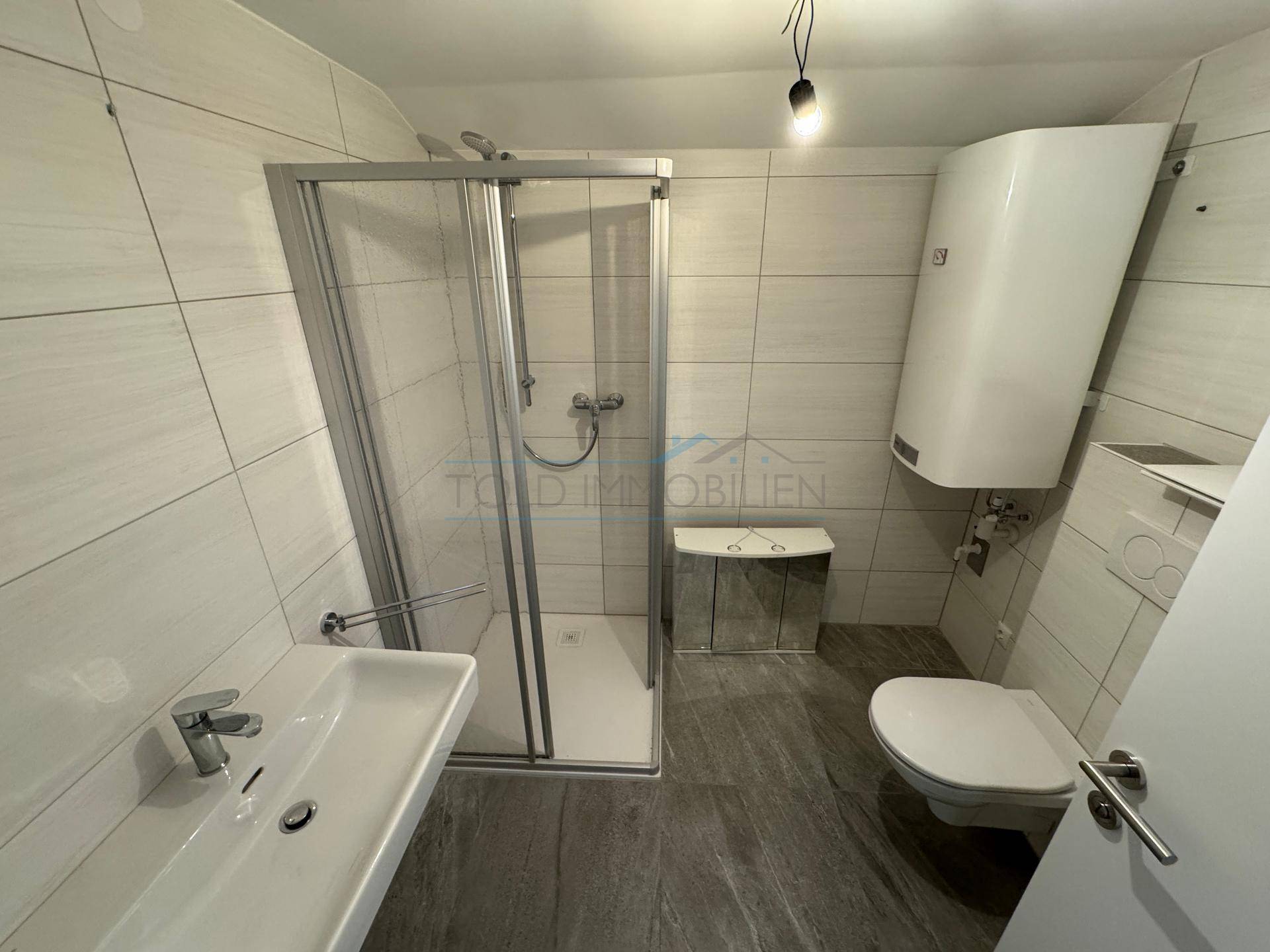 Modernes Badezimmer mit Duschkabine, Wand-WC und hellen Fliesen in gutem Zustand.