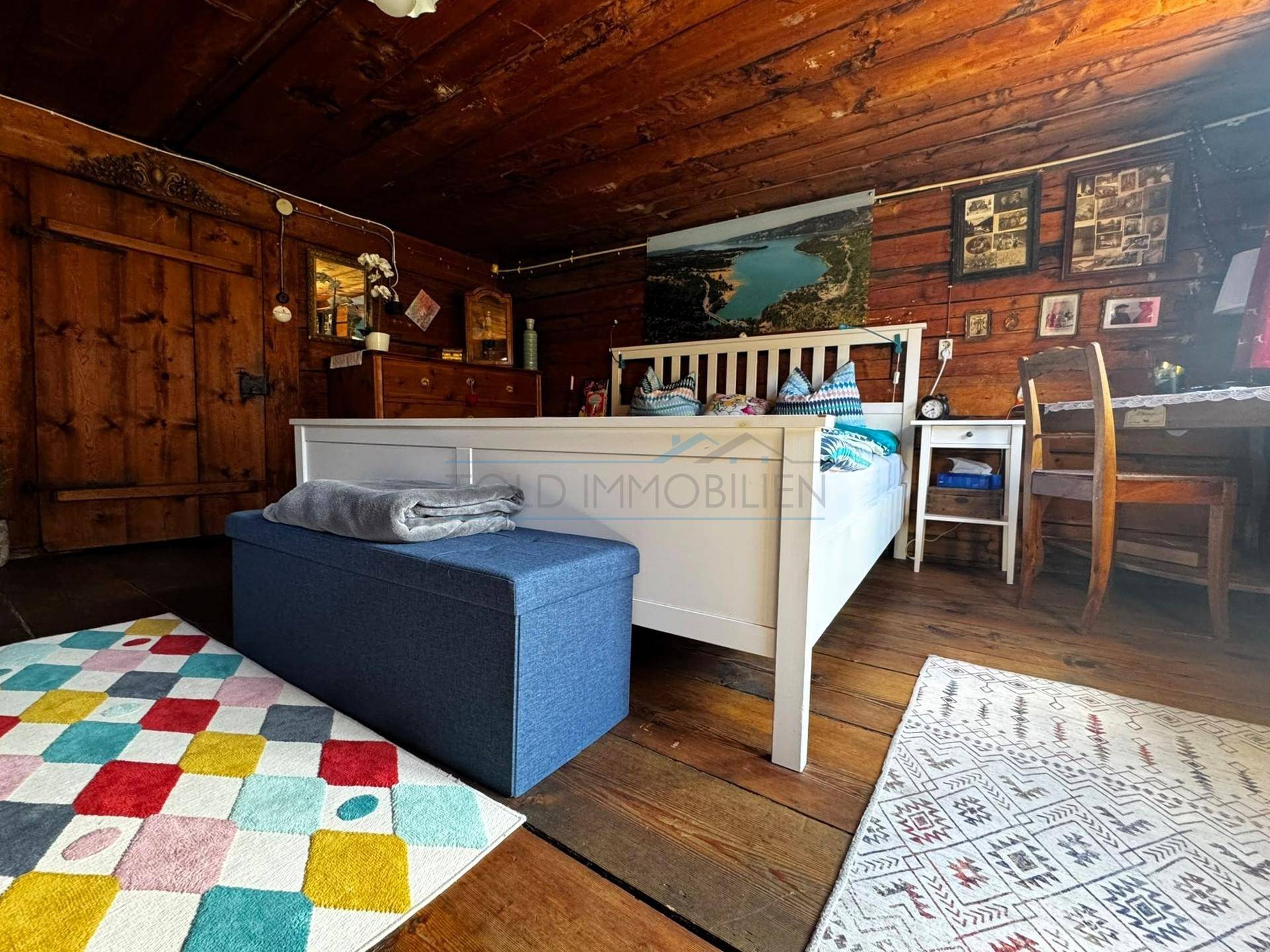 Helles Schlafzimmer mit Holzboden, weißem Bett und farbenfrohem Teppich.