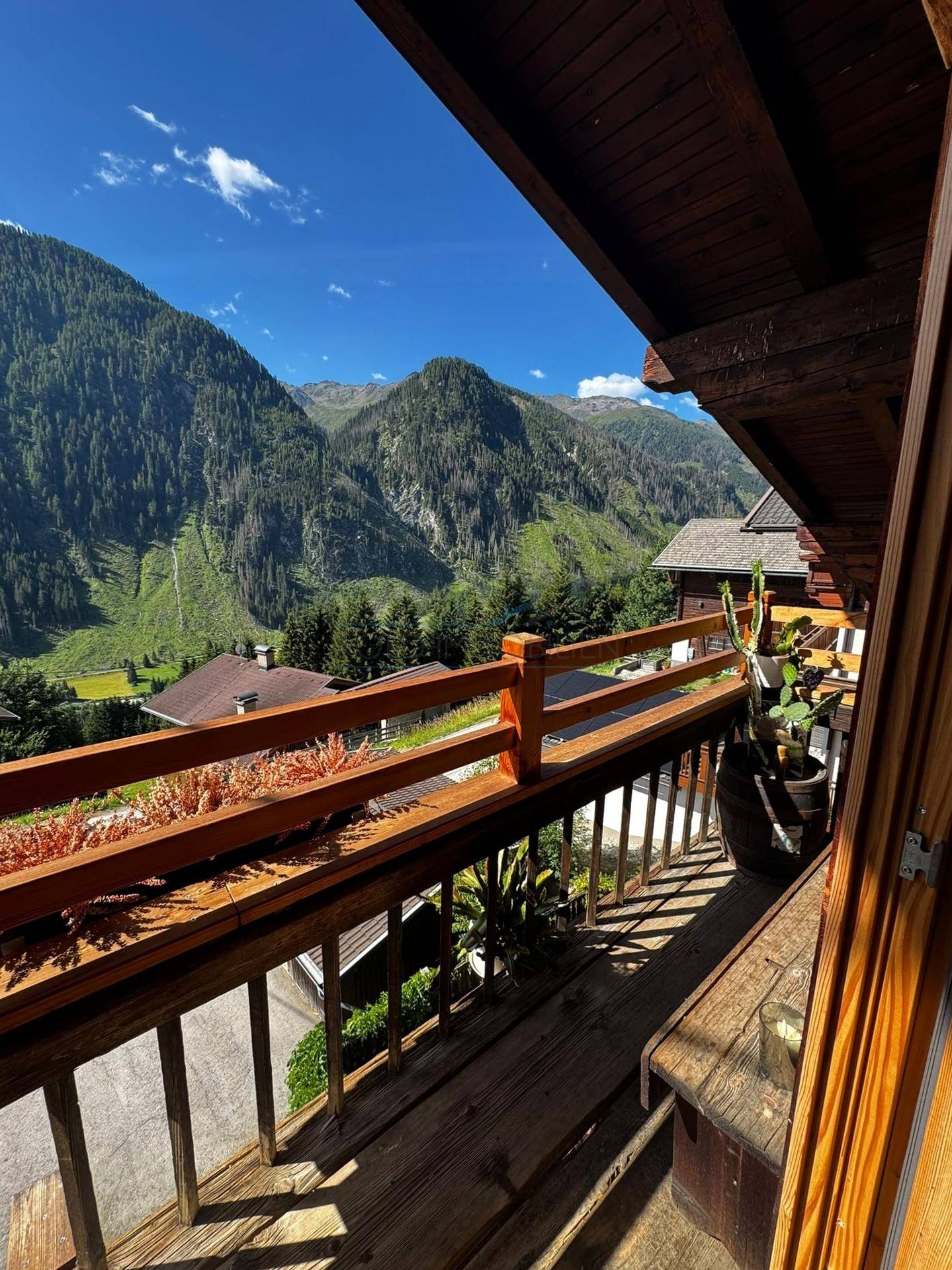 Sonniger Balkon mit Holzgeländer und atemberaubendem Blick auf die umliegenden Berge.