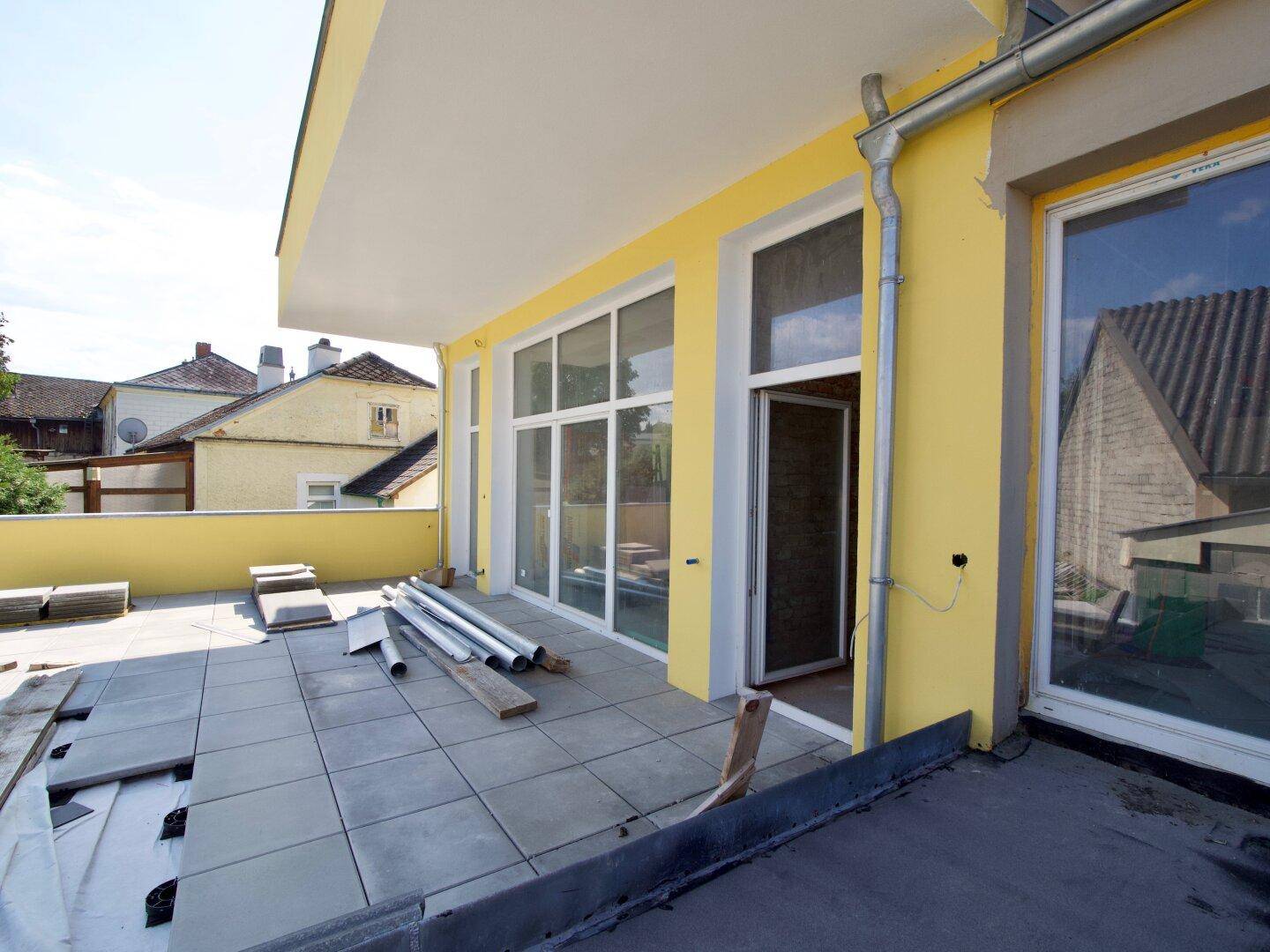 Im Bau befindliche Terrasse mit großen Fenstern und Baumaterialien.