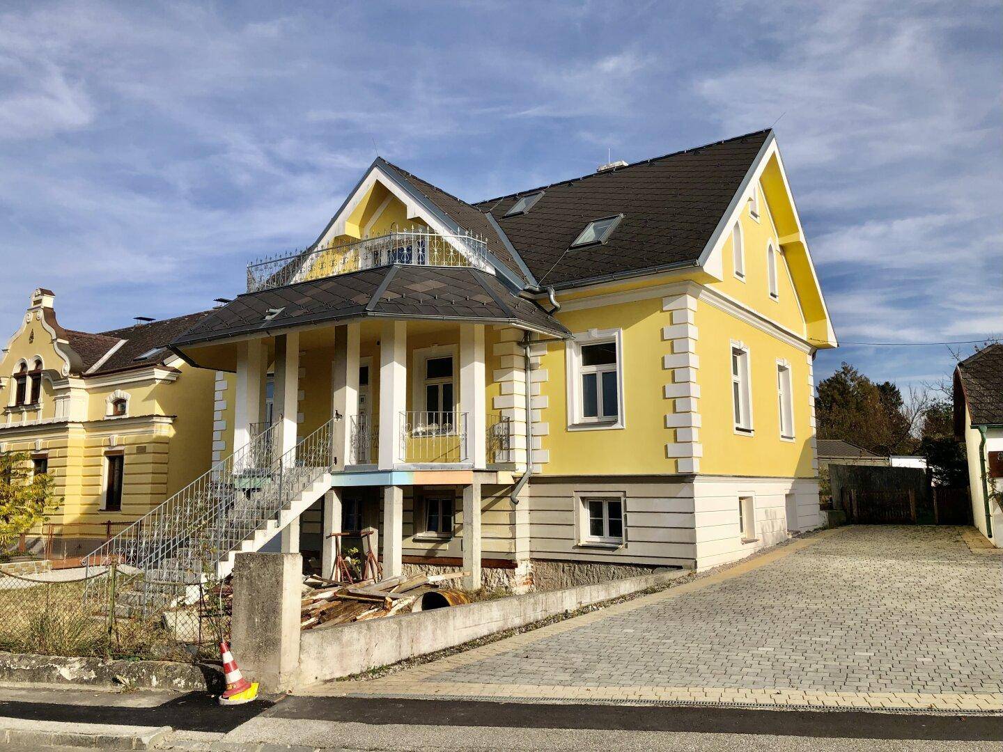 Ansicht des gelben Hauses mit Zufahrt und Baustellenbereich im Vordergrund.