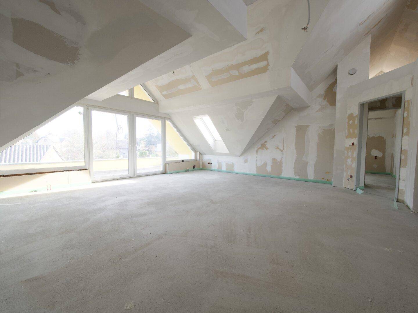 Geräumiger Dachboden im Rohbau mit schrägen Decken und Dachfenstern.