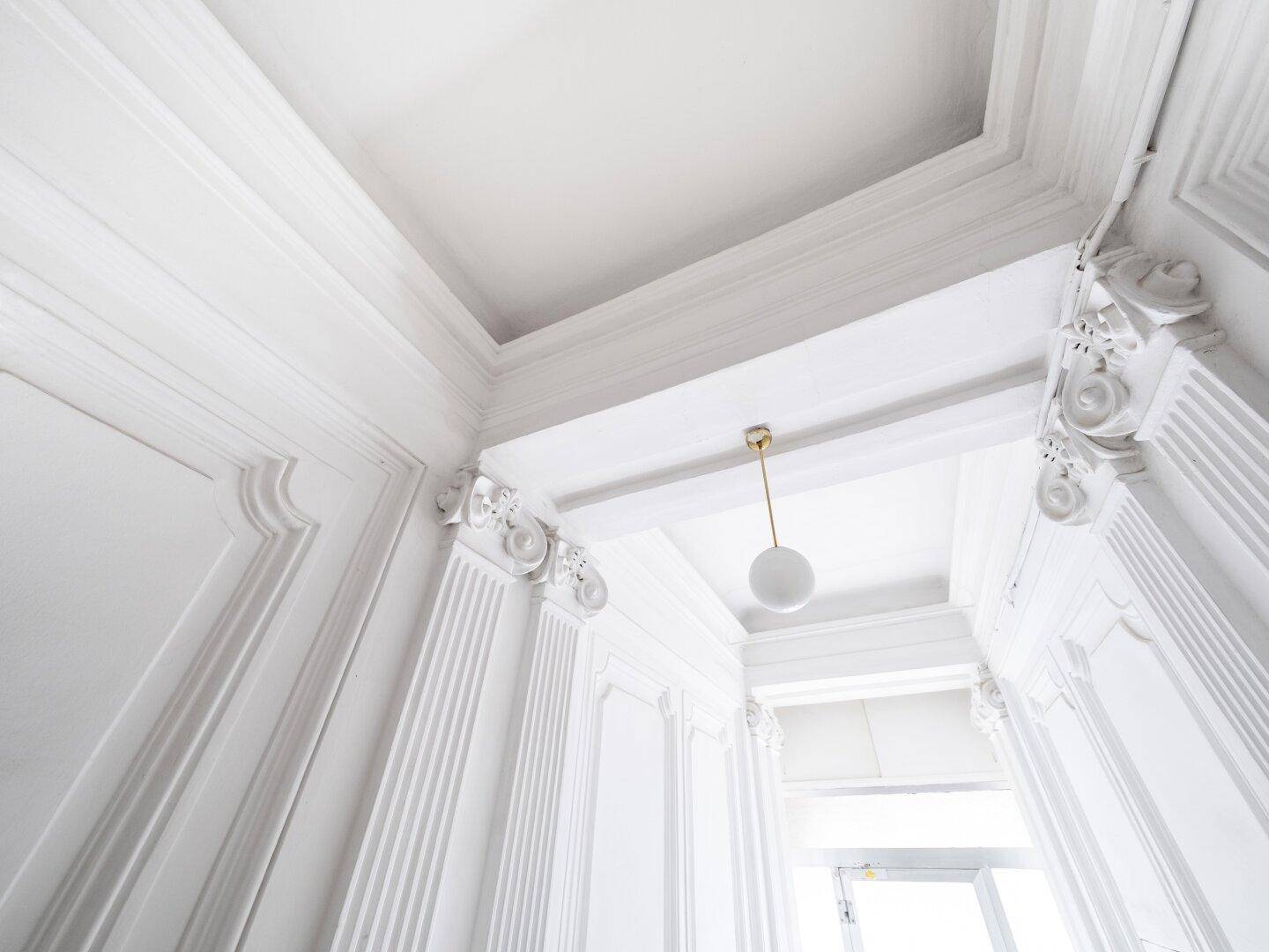 Elegante Stuckdecken und Wände mit klassischer Ornamentik und moderner Pendelleuchte.