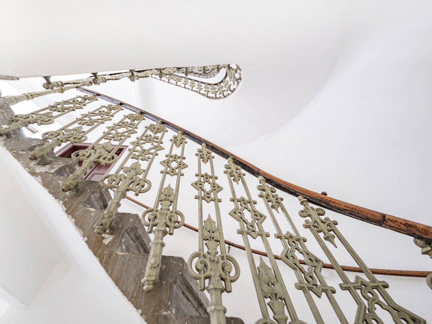 Historische Wendeltreppe mit kunstvollem schmiedeeisernem Geländer und Holzhandlauf.