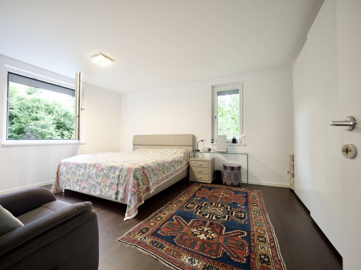 Gemütliches Schlafzimmer mit hellem Bett, zwei Fenstern und Blick ins Grüne.