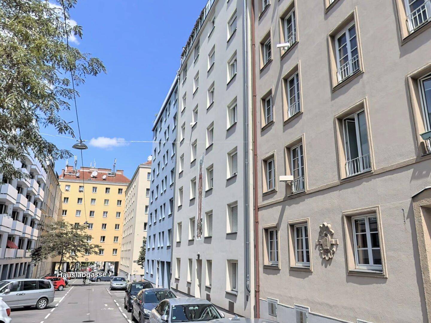 Ansicht einer städtischen Straße mit mehrstöckigen Wohngebäuden und geparkten Autos.