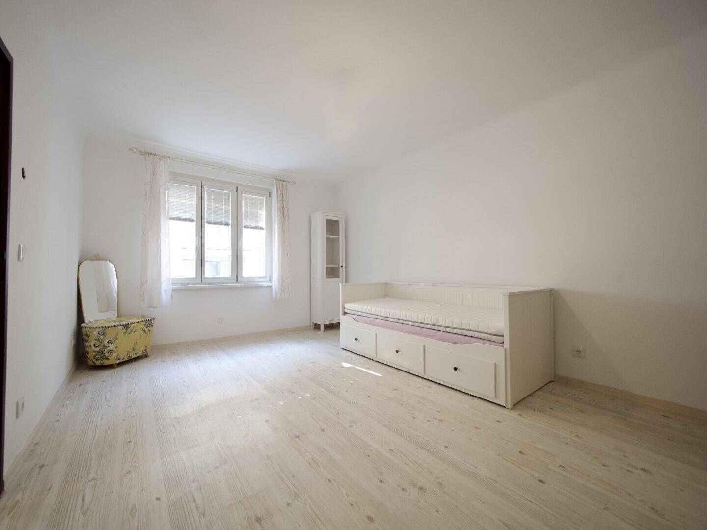 Geräumiges Schlafzimmer mit hellem Holzboden, Tagesbett und viel natürlichem Licht.