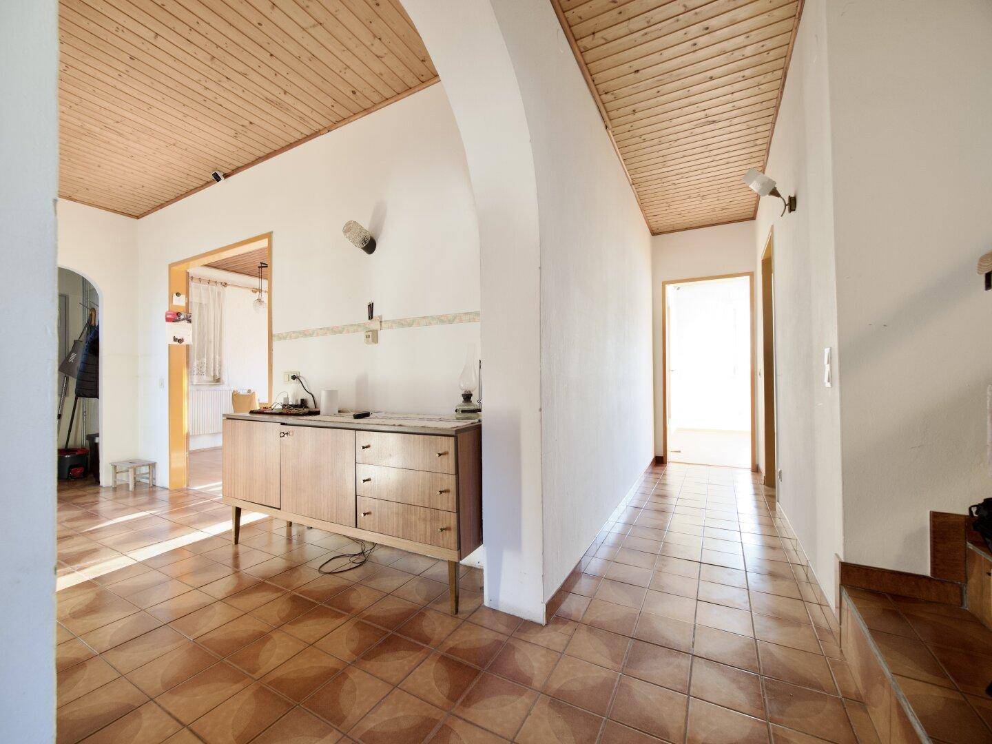 Geräumiger Flur mit Fliesenboden und Holzdecke, der einen einladenden Eingangsbereich bildet.
