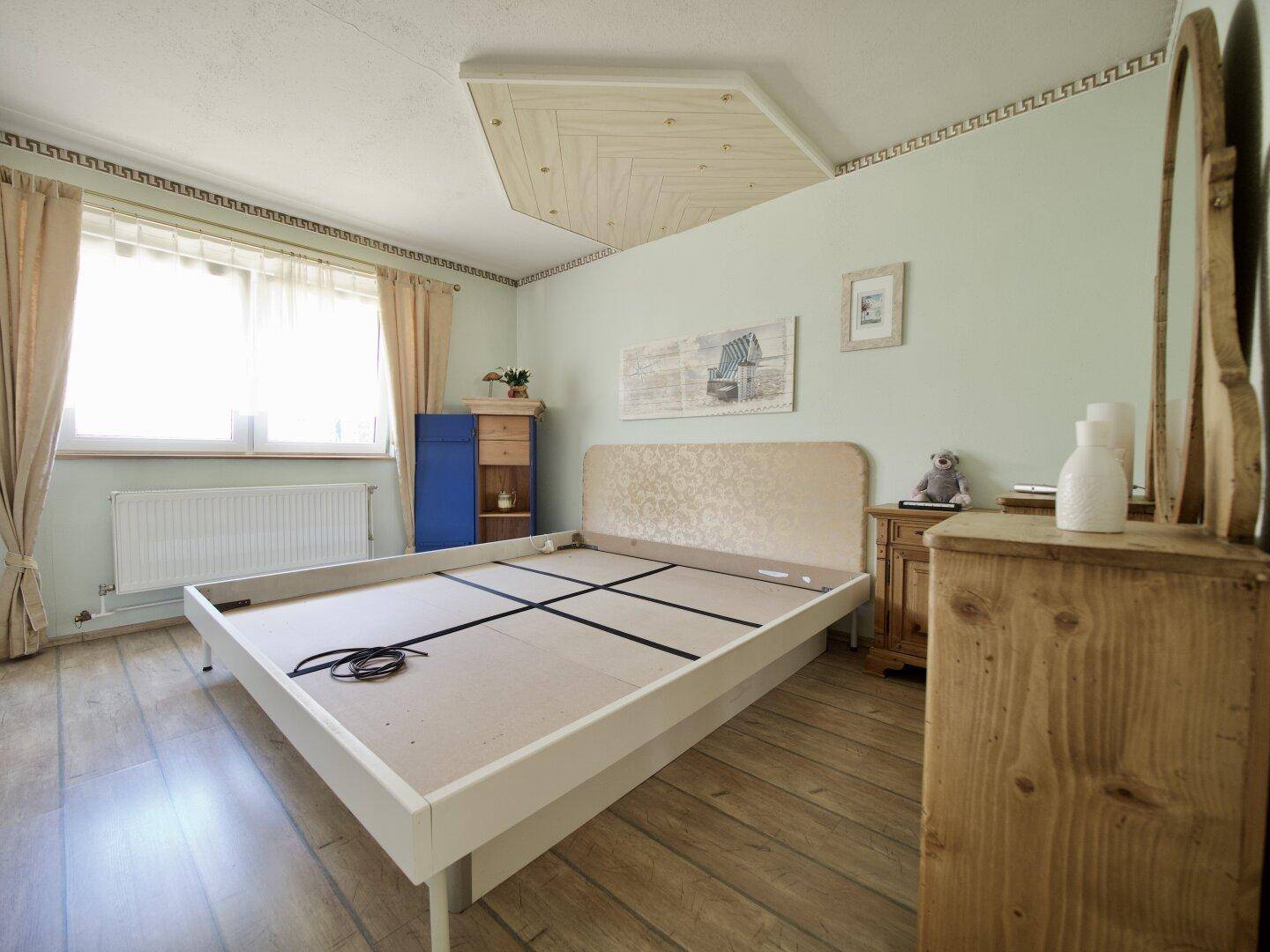 Ein helles Schlafzimmer mit Holzboden, einem Bettgestell und einem Holzschrank.