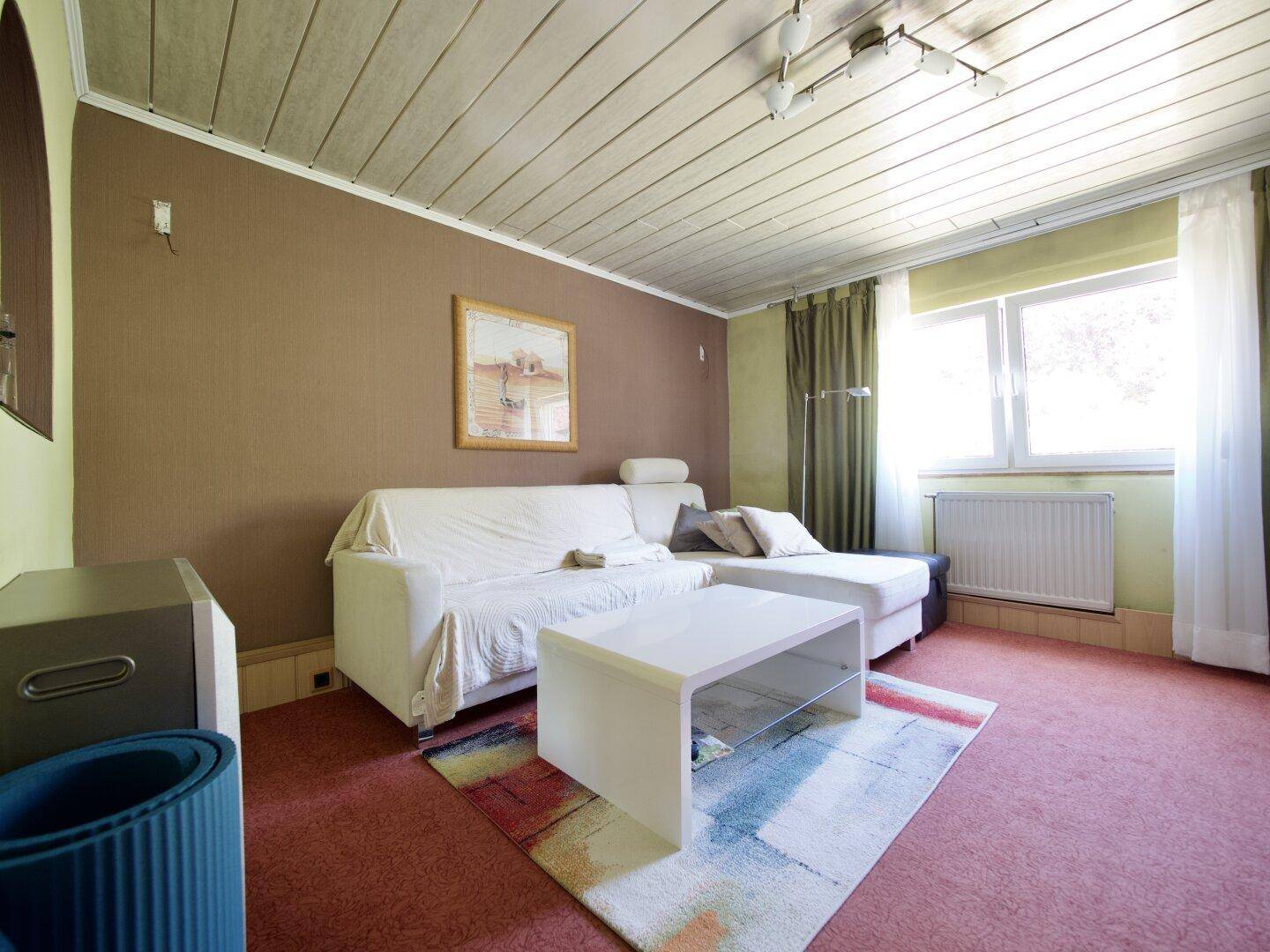 Ein gemütliches Wohnzimmer mit Teppichboden, weißem Sofa und Holzdecke.