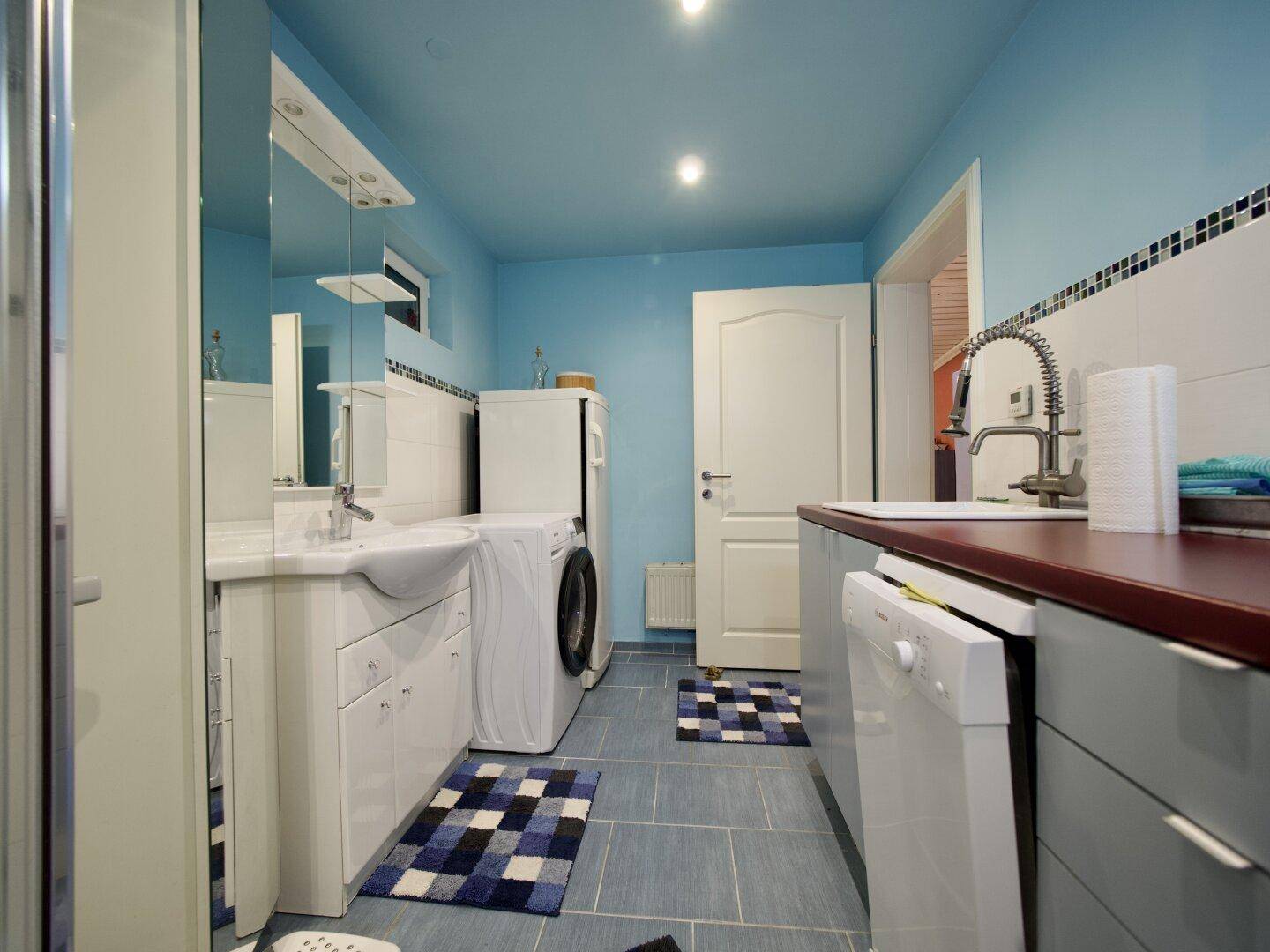 Ein funktionaler Hauswirtschaftsraum mit Waschmaschine, Trockner und Waschbecken in blau gestrichenen Wänden.
