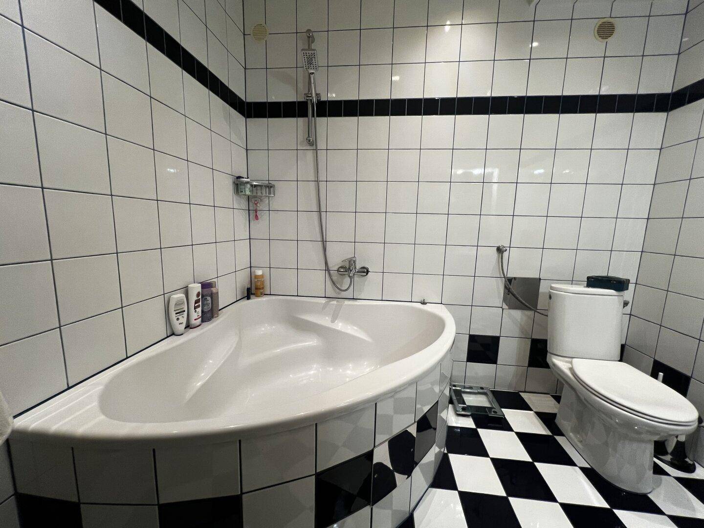 Badezimmer mit schwarz-weiß gefliestem Boden, Eckbadewanne und Toilette.