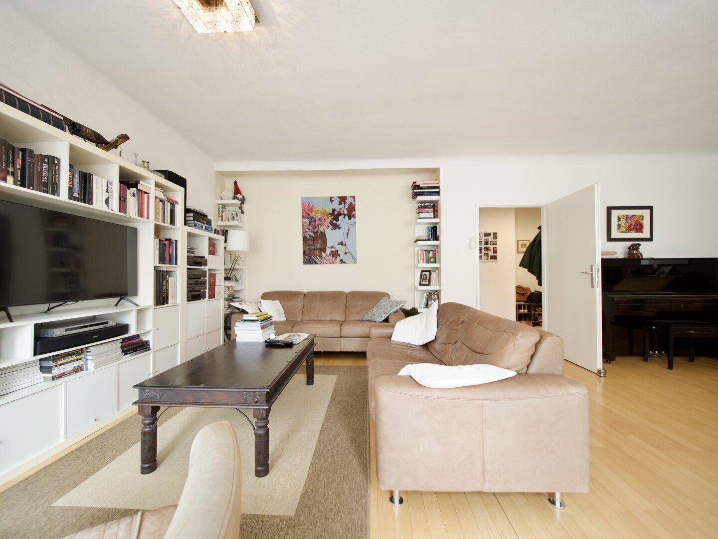 Geräumiges Wohnzimmer mit Bücherregalen, Fernseher und einem Klavier im Hintergrund.