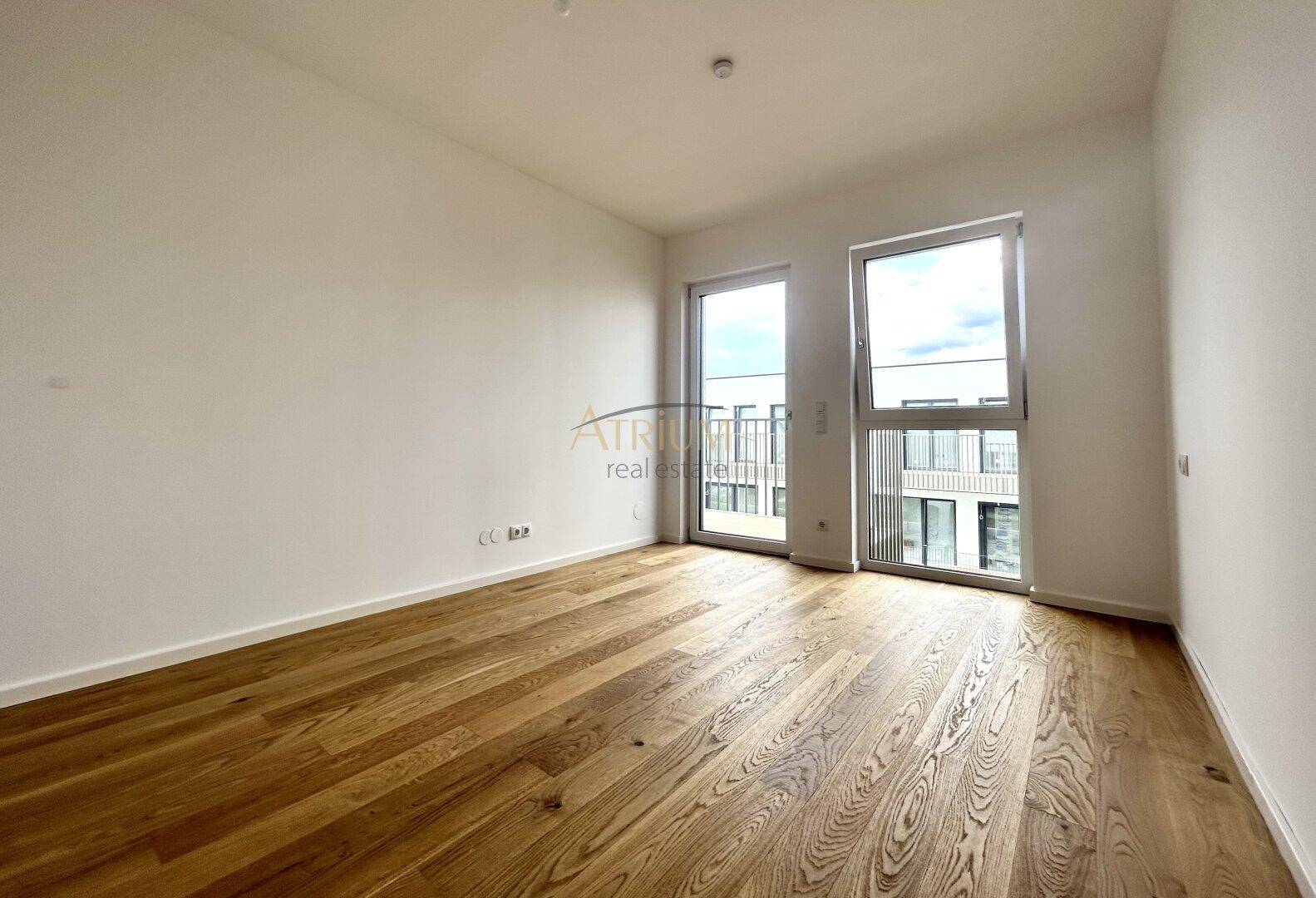Geräumiges Zimmer mit Eichenparkett und viel Tageslicht durch große Fenster.