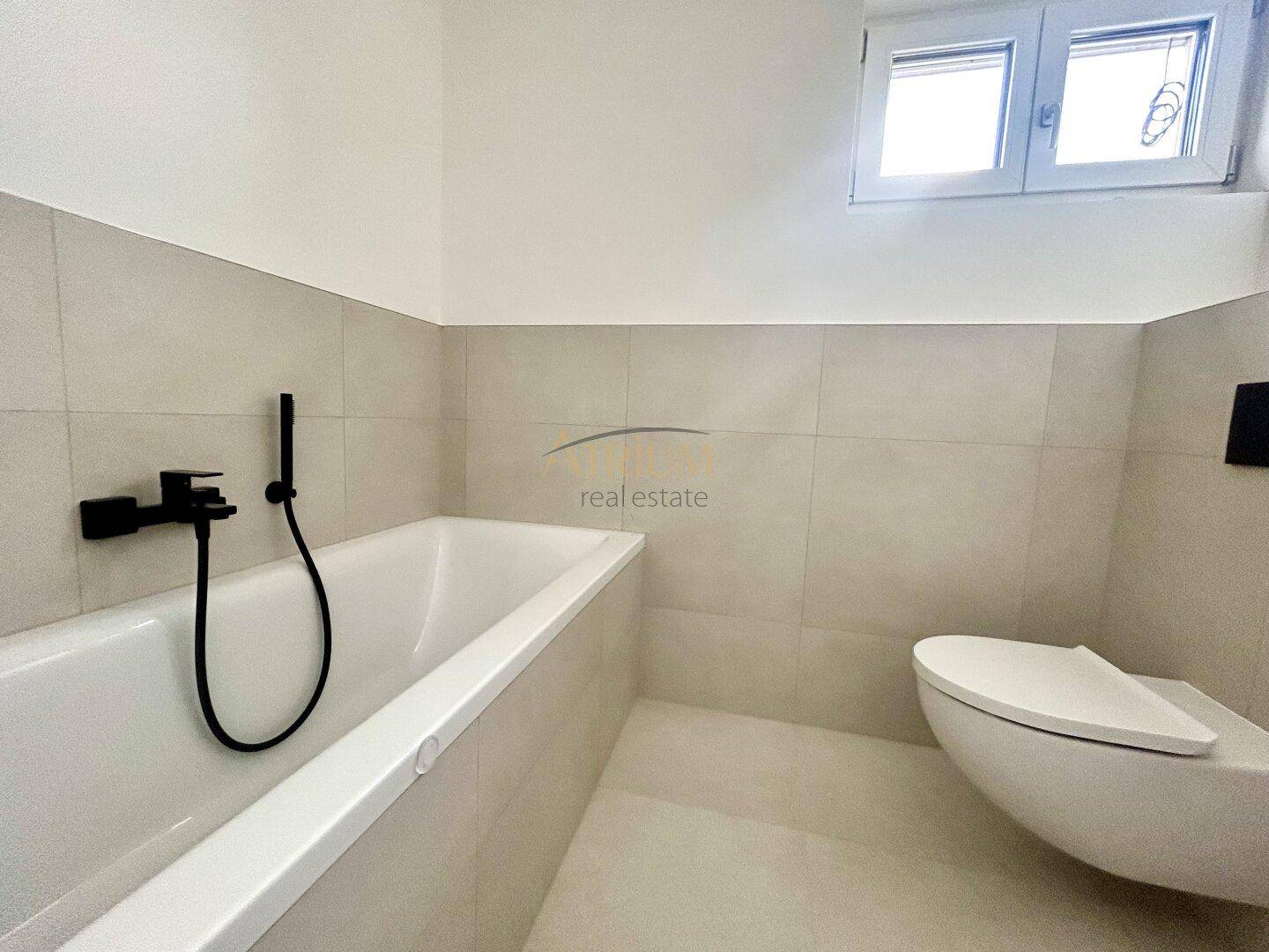 Modernes Badezimmer mit Badewanne, wandhängendem WC und Fenster.