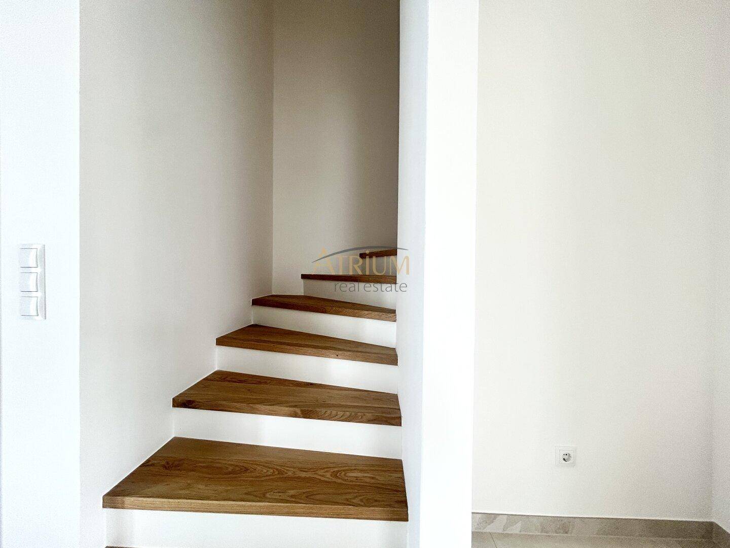 Moderne Holztreppe mit weißen Setzstufen in einem hellen Treppenhaus.