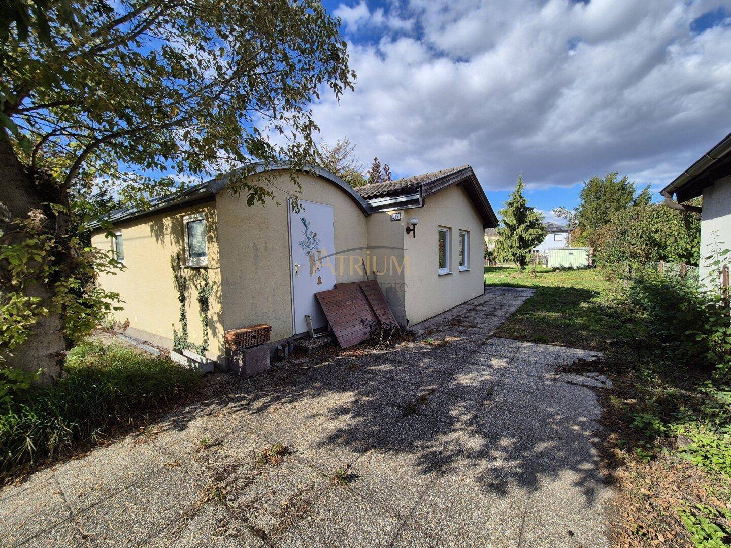 Kleines Haus mit gepflastertem Vorplatz und angrenzendem, naturbelassenem Gartenbereich.