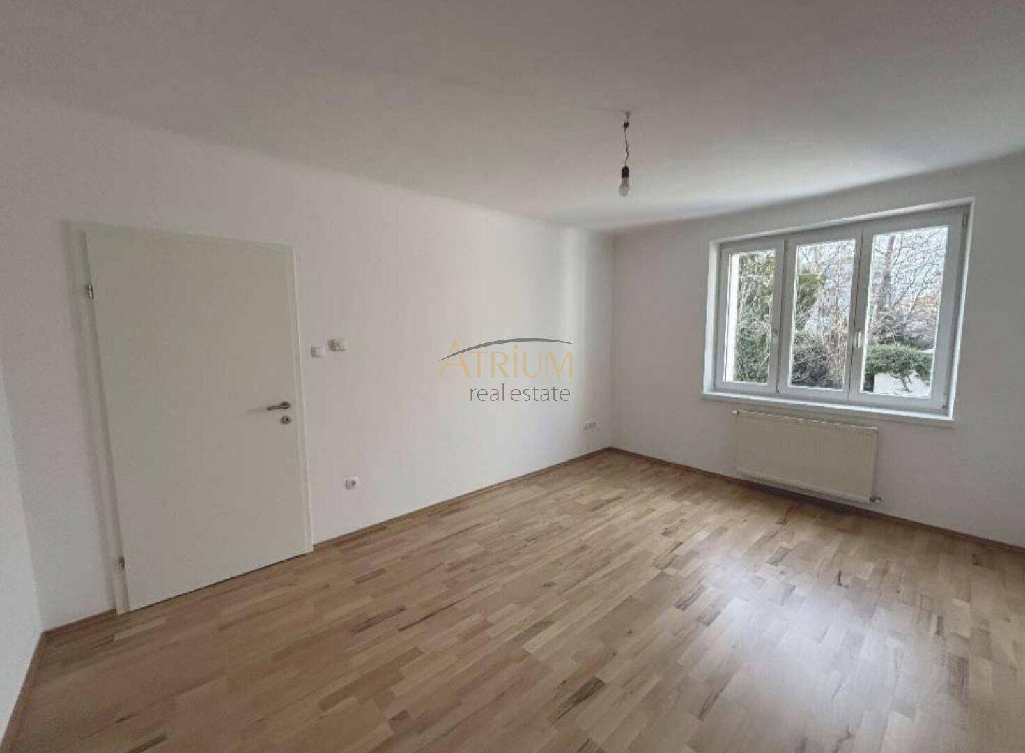 Geräumiges Zimmer mit Holzboden und Fenster, das viel Tageslicht hereinlässt.