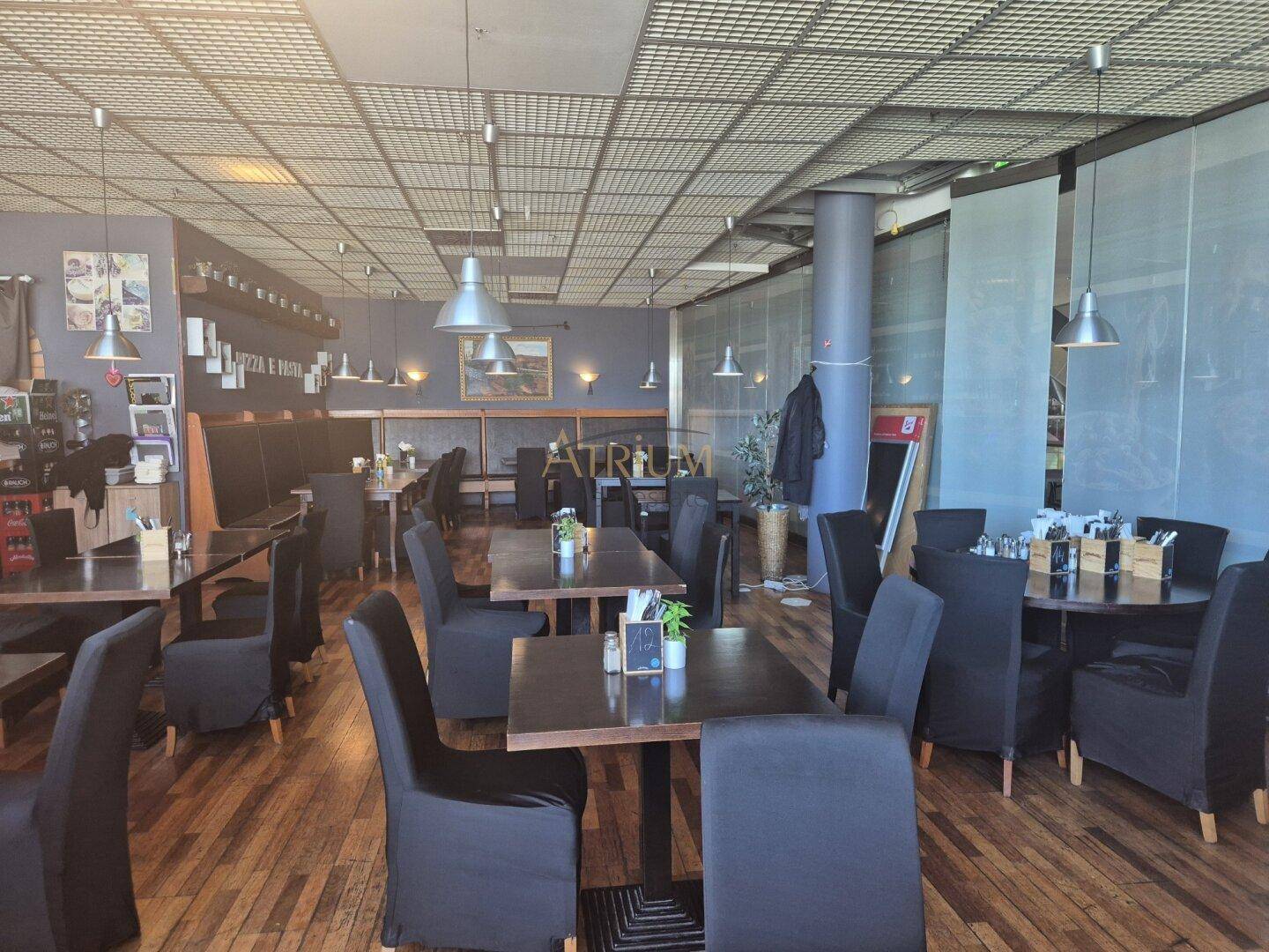 Geräumiger Restaurantbereich mit dunklen Holztischen, schwarzen Stühlen und großen Fenstern.