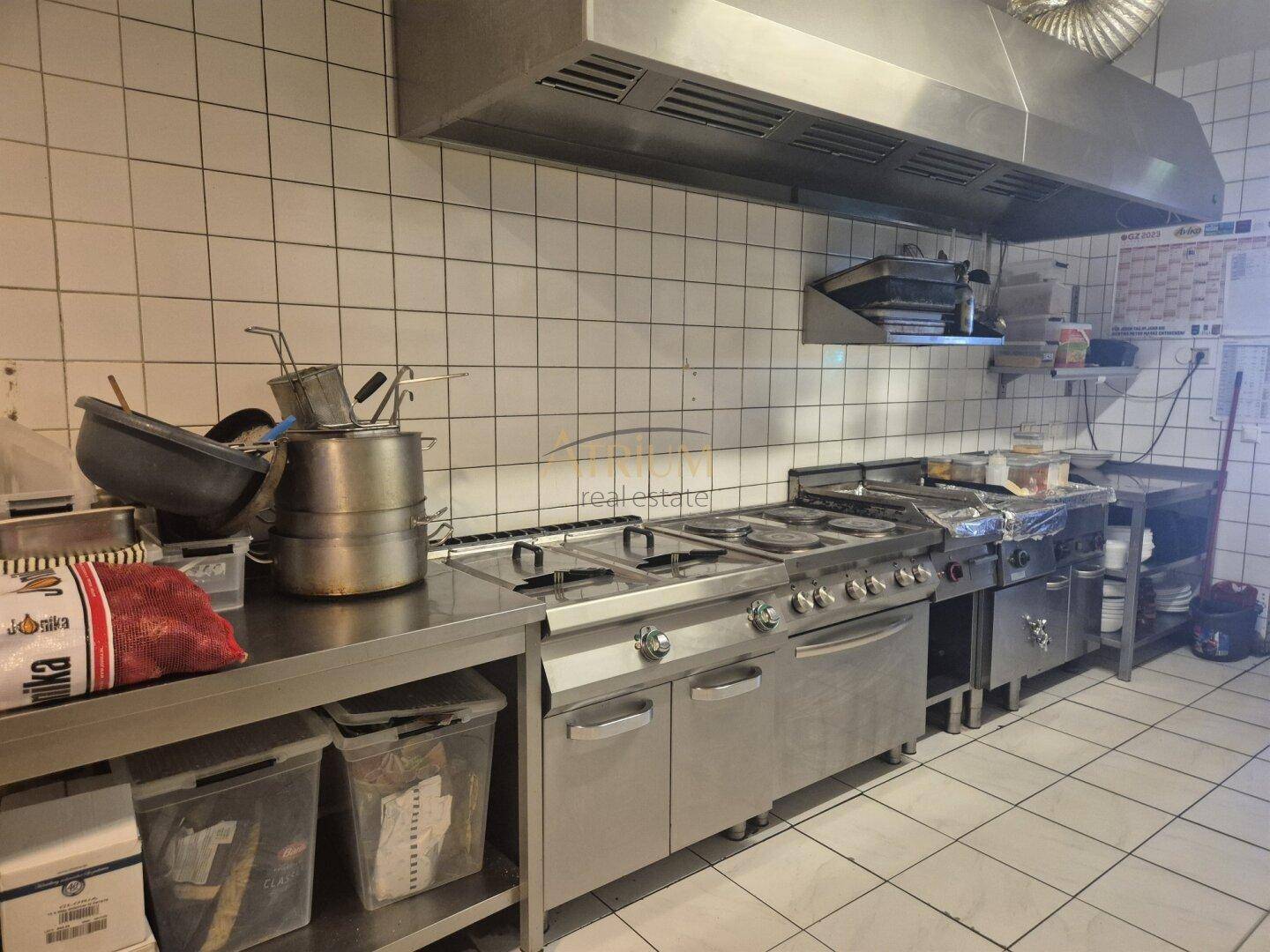 Industrielle Küche mit professionellen Kochfeldern, Dunstabzugshaube und Edelstahl-Arbeitsflächen.