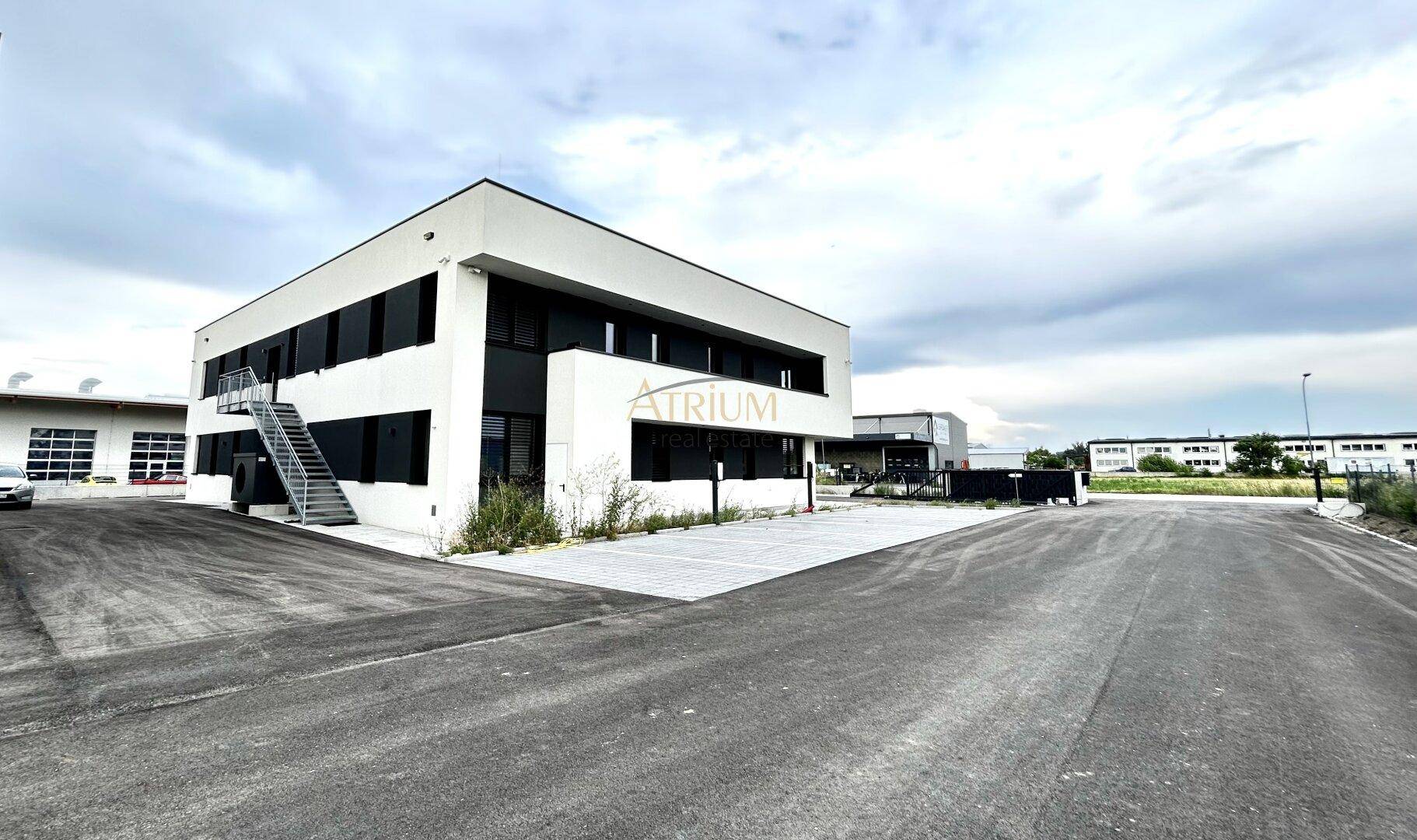 Modernes Bürogebäude mit weißer Fassade und dunklen Fensterbändern, umgeben von einer asphaltierten Fläche.