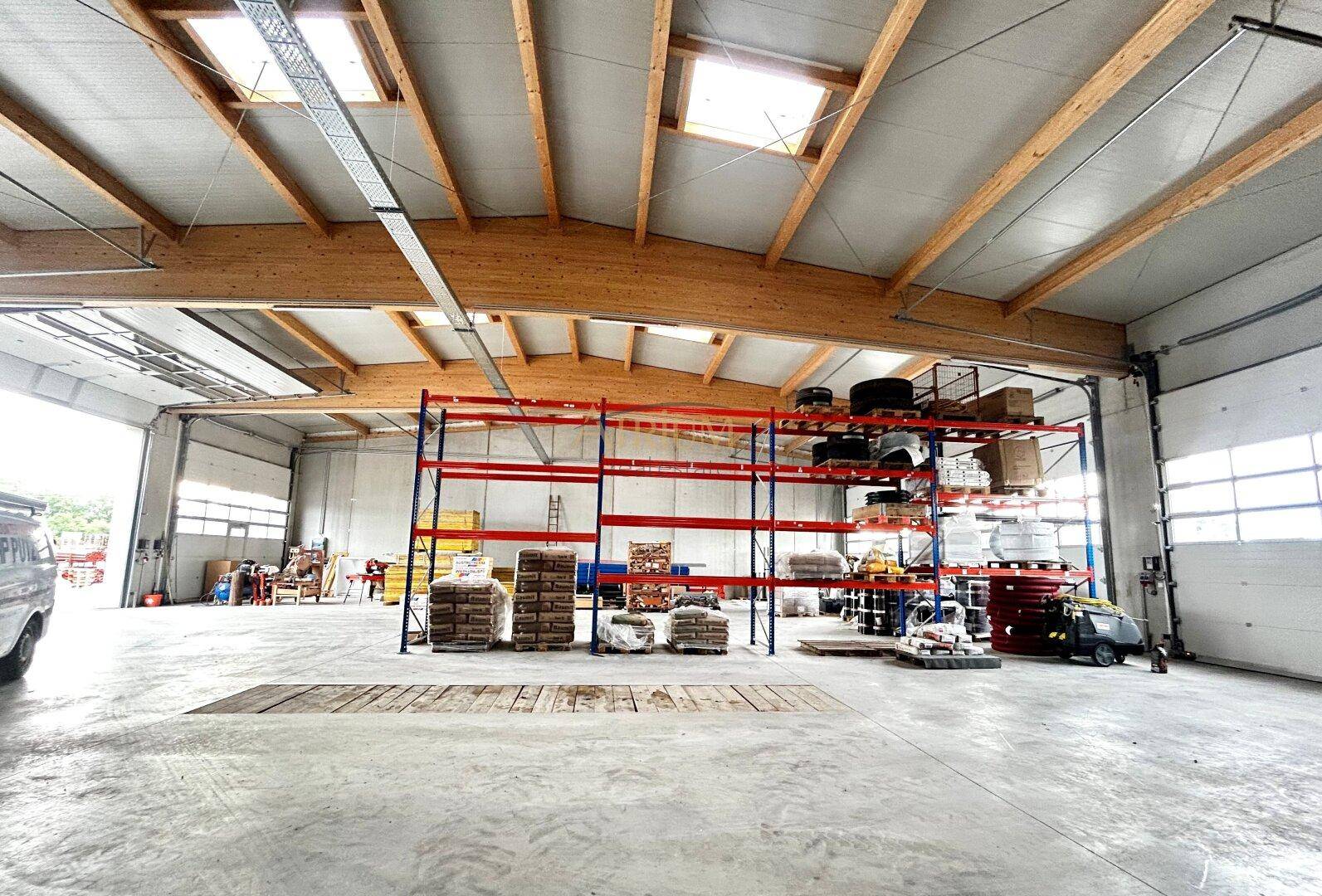 Große Lagerhalle mit hohen Holzdecken, Oberlichtern und Regalsystemen für Lagerung.