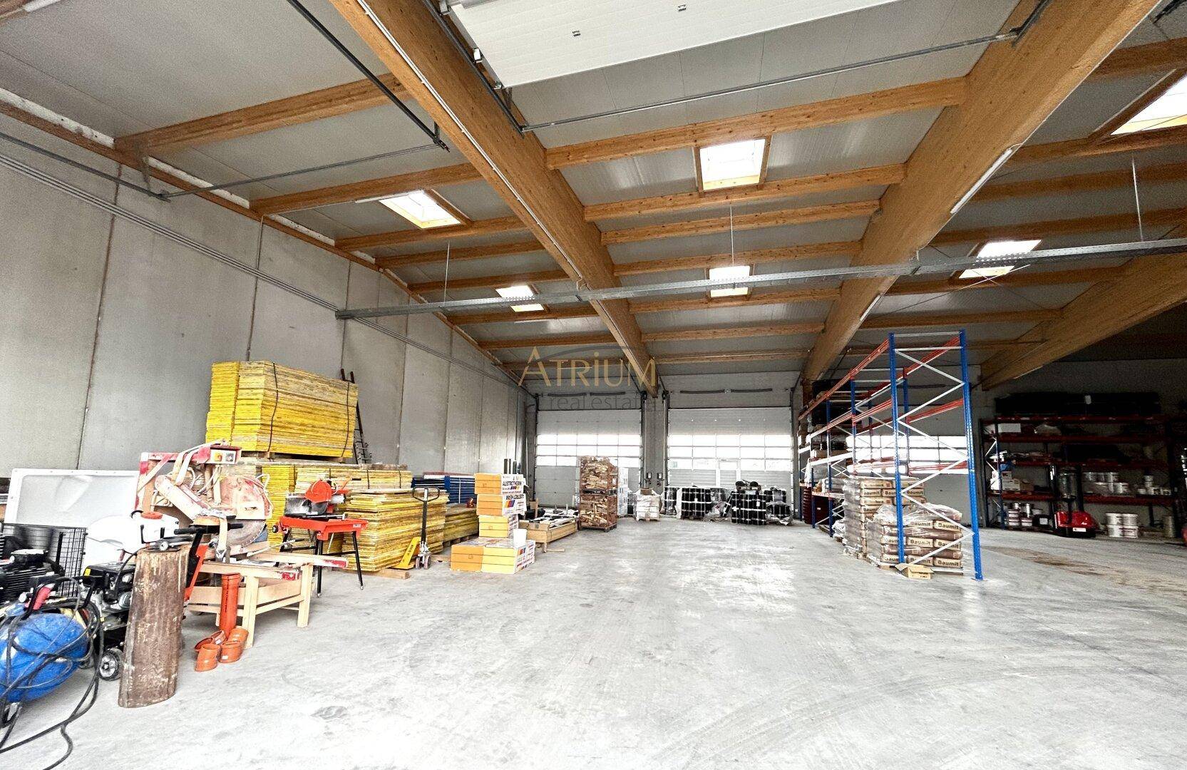 Geräumige Lagerhalle mit sichtbaren Holzträgern, Oberlichtern und verschiedenen Baumaterialien.