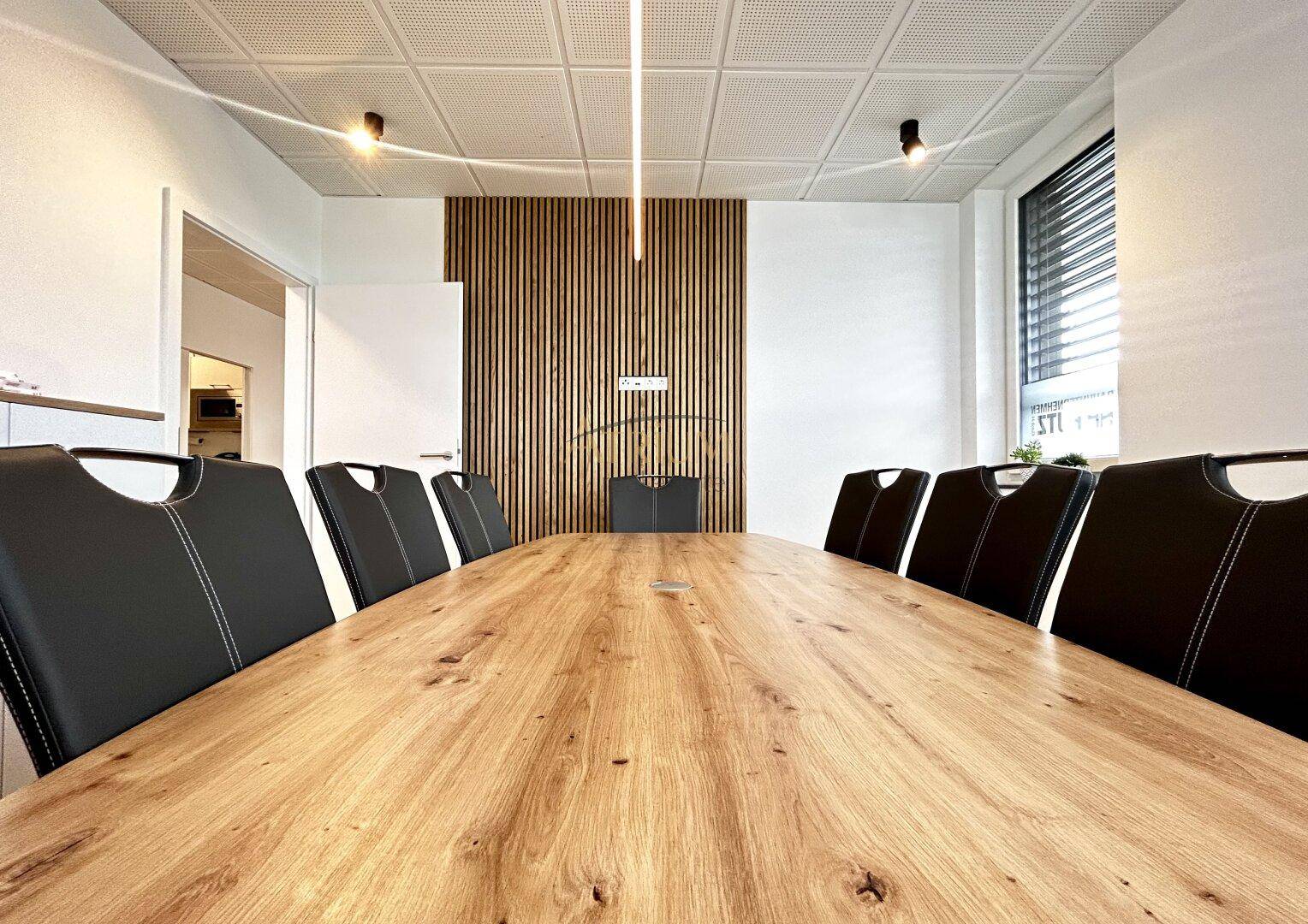 Geräumiger Konferenzraum mit großem Holztisch, modernen Deckenleuchten und einer stilvollen Holzwand.