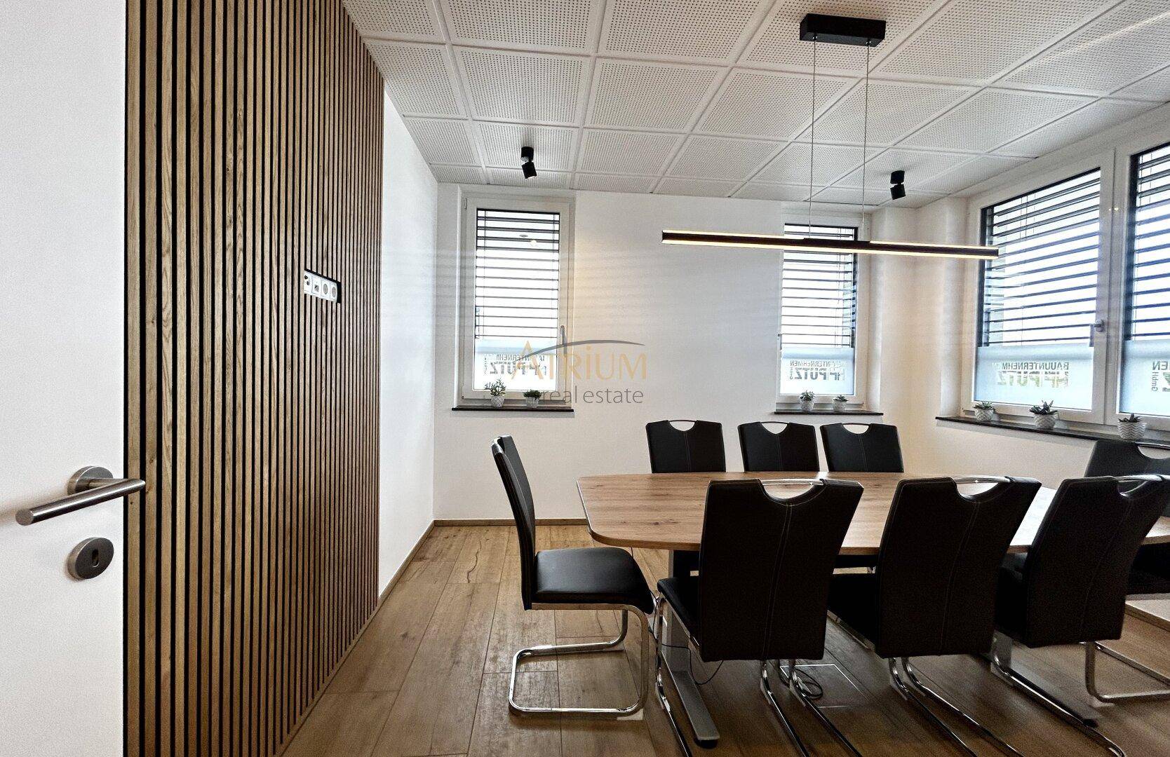 Heller Konferenzraum mit mehreren Fenstern, Holzboden und einer vertikalen Holzverkleidung an der Wand.