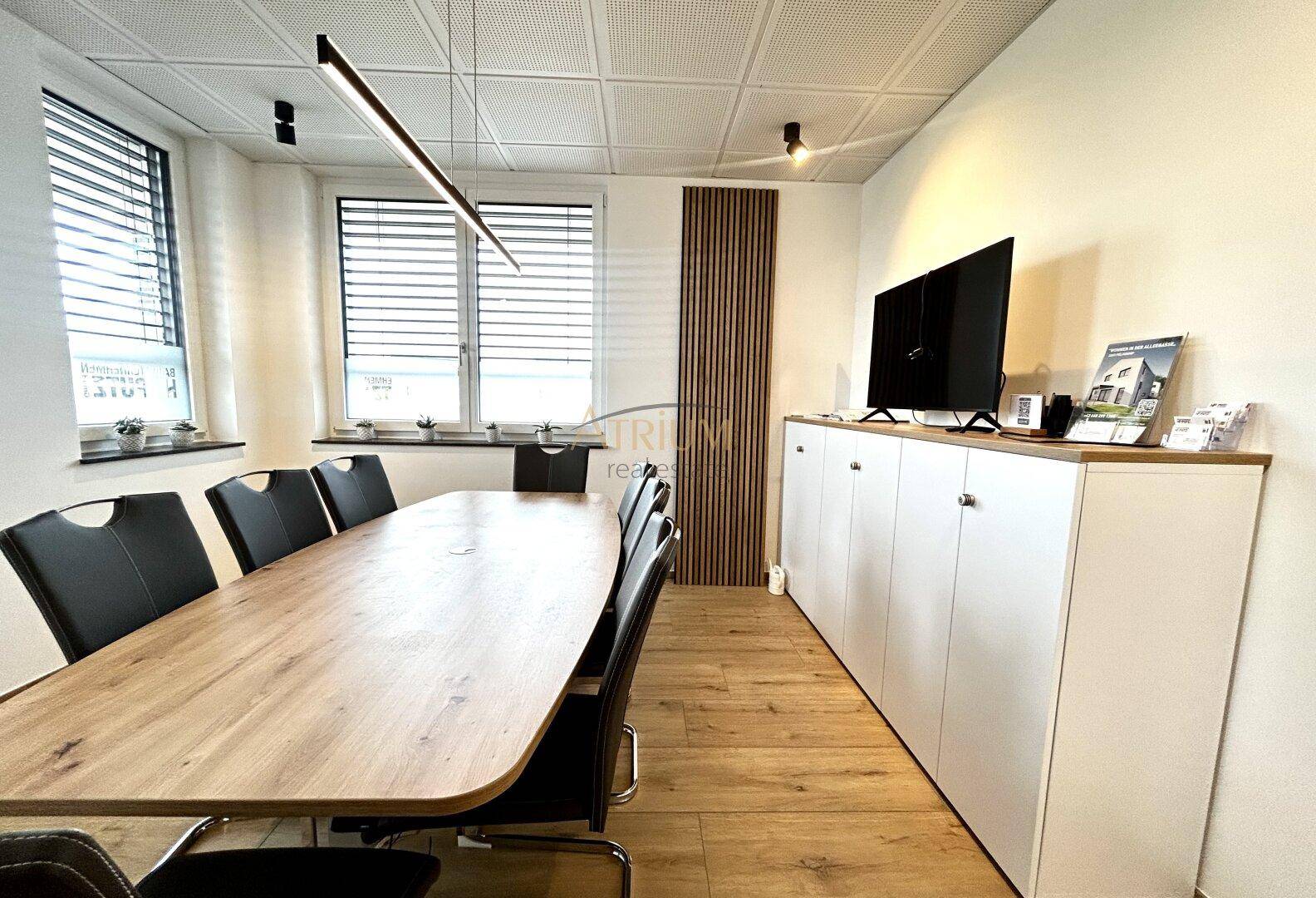 Moderner Konferenzraum mit langem Holztisch, schwarzen Stühlen und einer Holzwandverkleidung.
