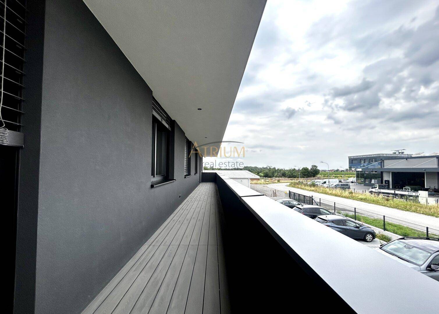 Langer Balkon mit Holzboden und Blick auf eine Straße mit parkenden Autos und umliegende Gebäude.