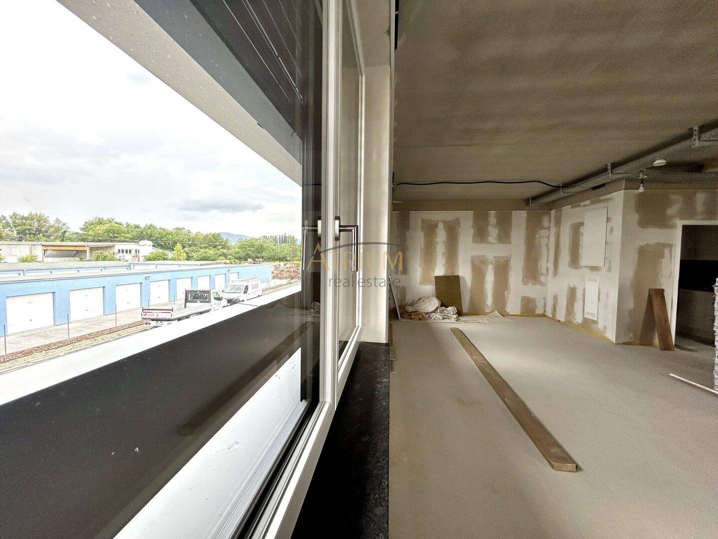 Unfertiger Büroraum mit großen Fenstern, die einen Blick auf die Umgebung und andere Gebäude bieten.