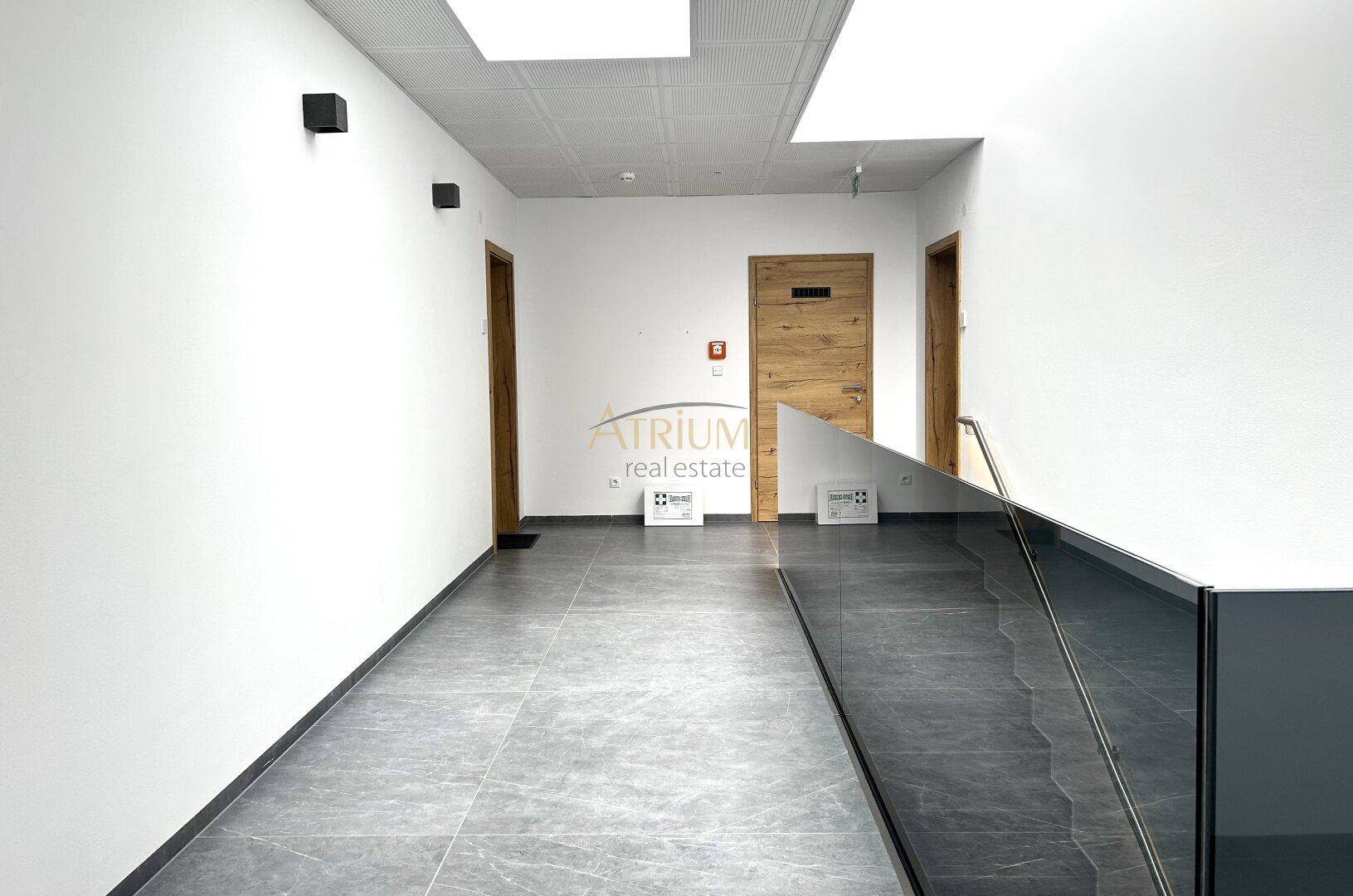 Geräumiger Flur mit hellen Wänden, grauen Fliesen und einer modernen Treppe mit Glasgeländer.