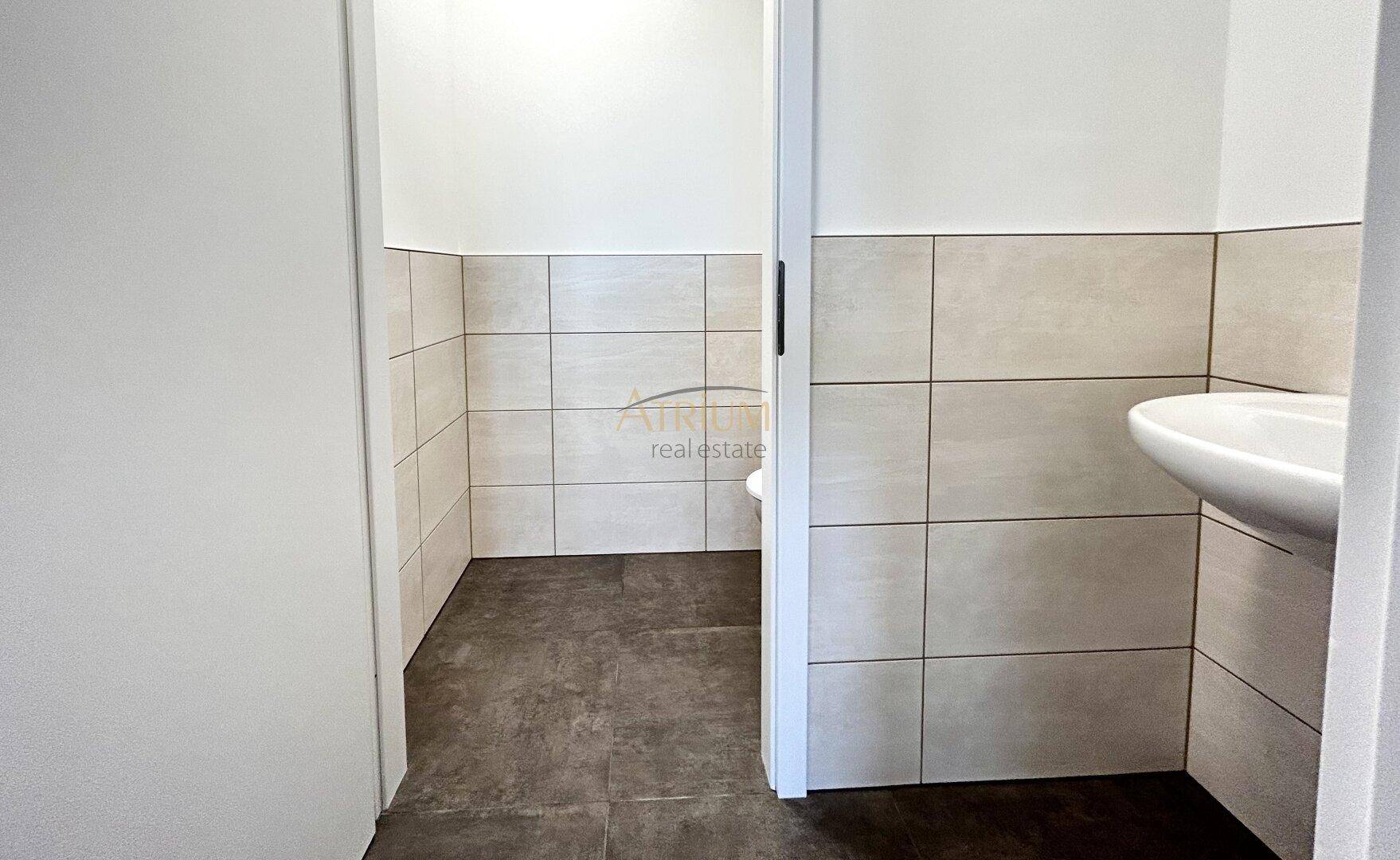 Modern geflieste Gästetoilette mit hellem Waschbecken und neutralen Wand- und Bodenfliesen.