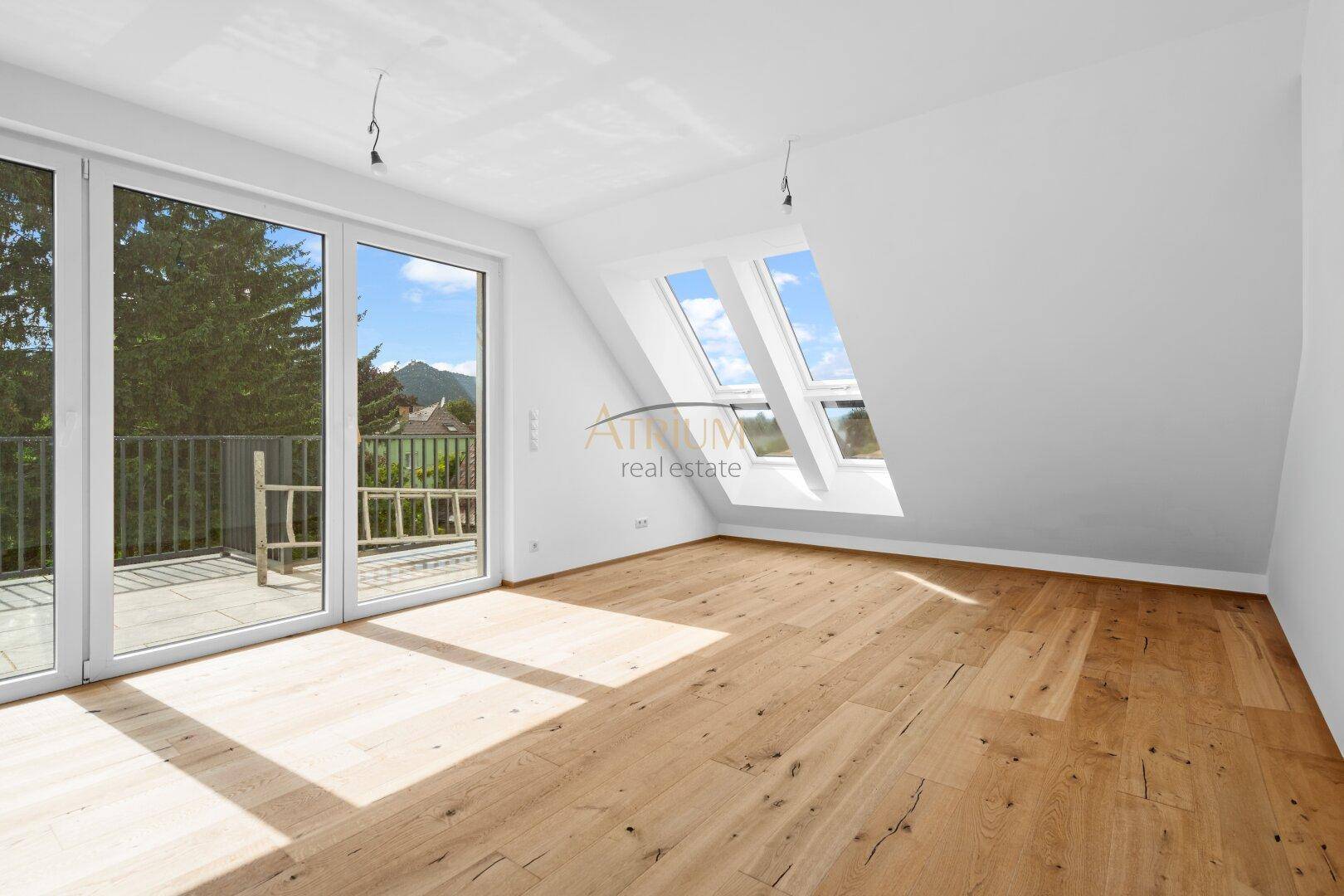 Lichtdurchfluteter Raum mit Holzboden, Zugang zur Terrasse und mehreren Dachfenstern.